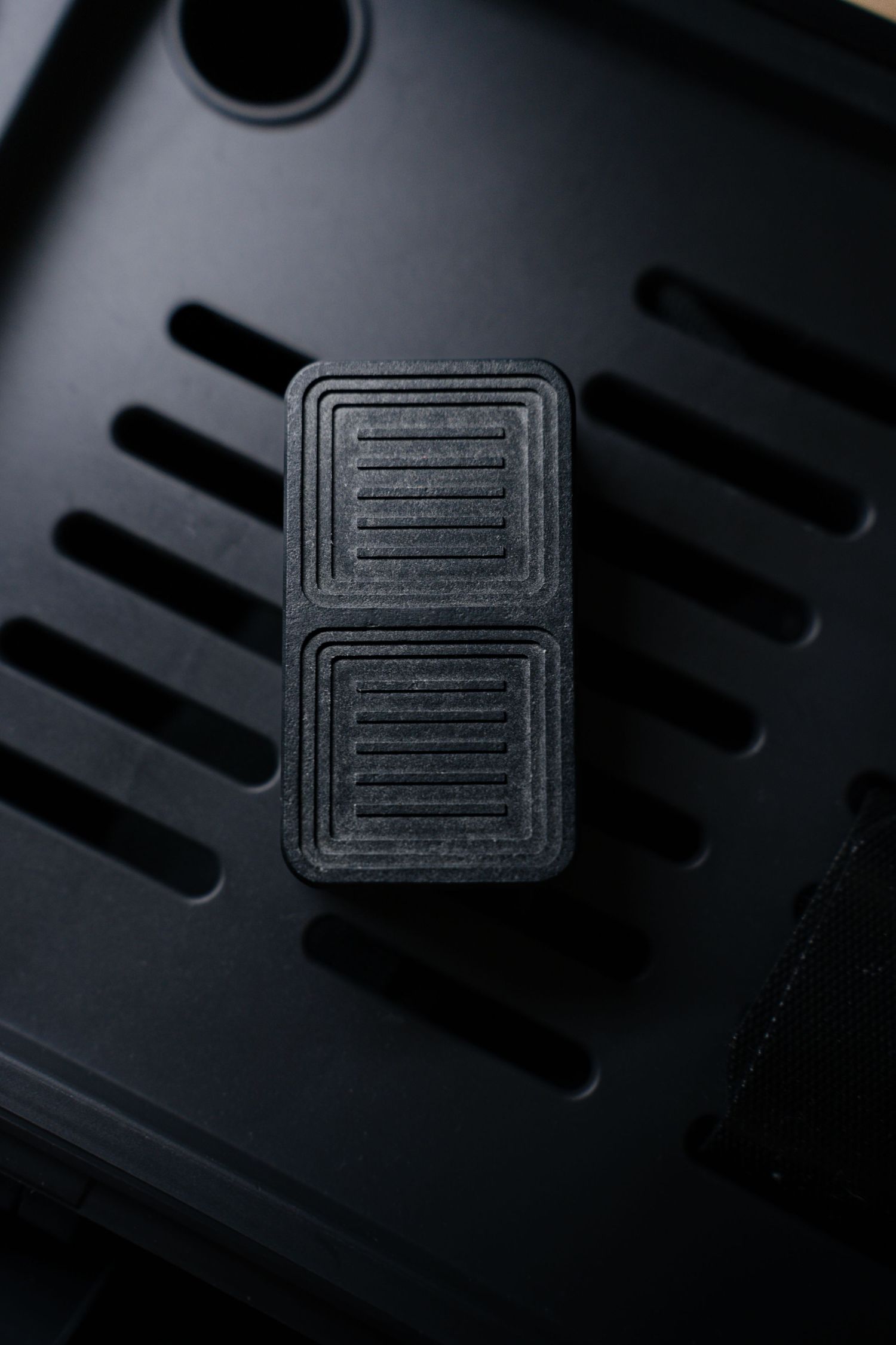 Product photography of Black ribbed rubber computer case foot pad placed on dark PC case surface.