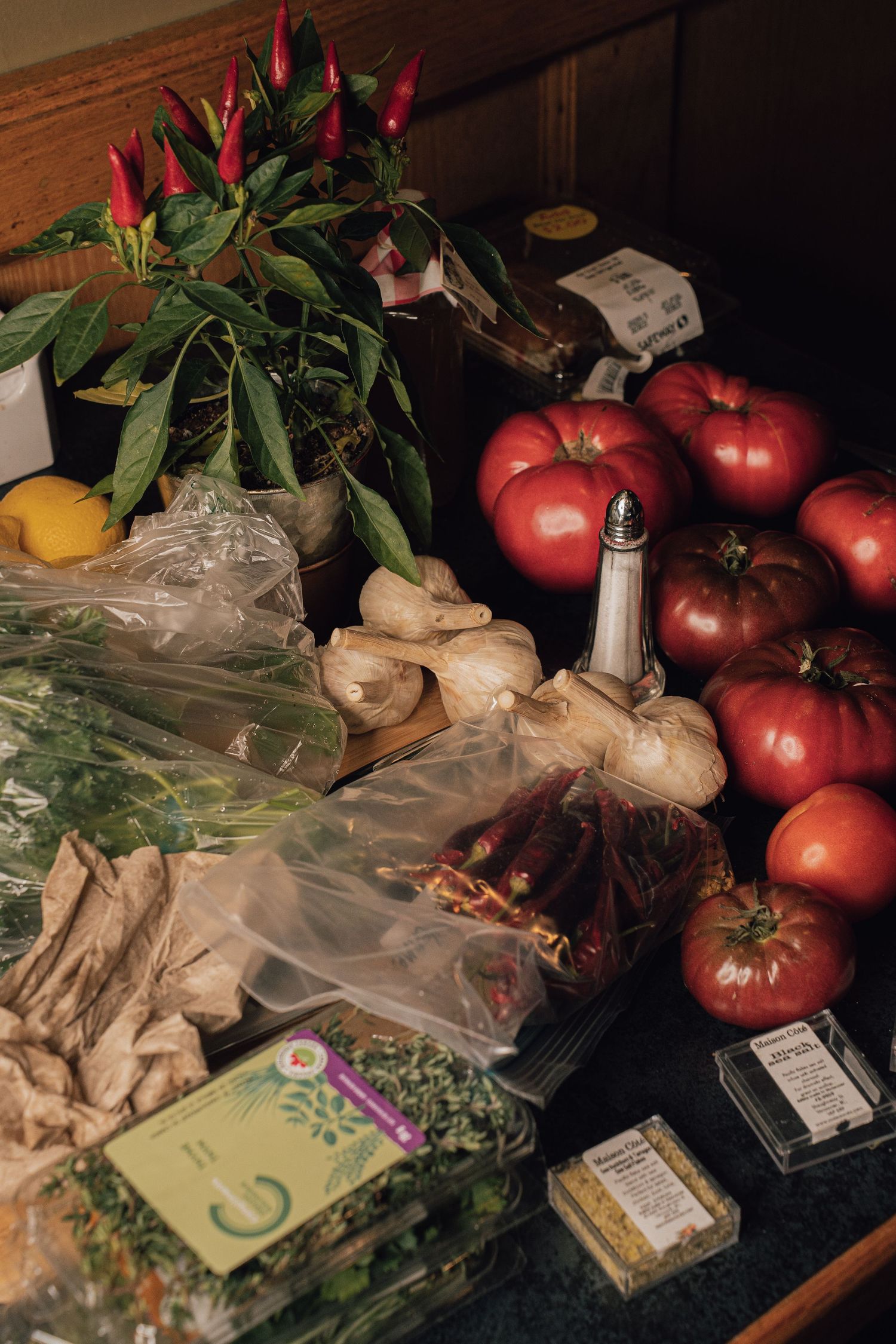 Fresh ingredients including heirloom tomatoes, chili peppers, ginger, and herbs on a wooden surface.