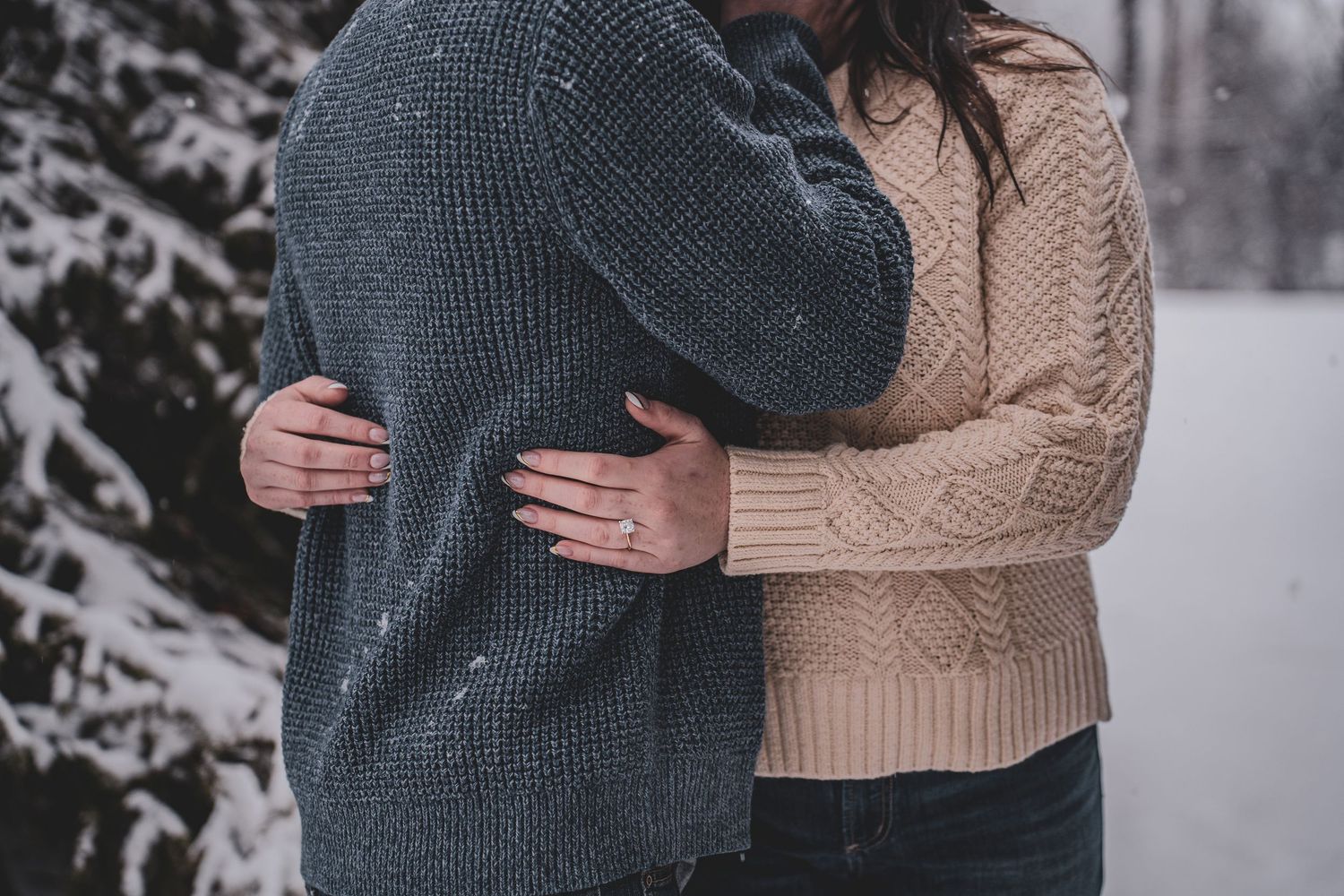 Close-up of couple embracing in winter, showing hands wrapped around each other in cozy knit sweaters.