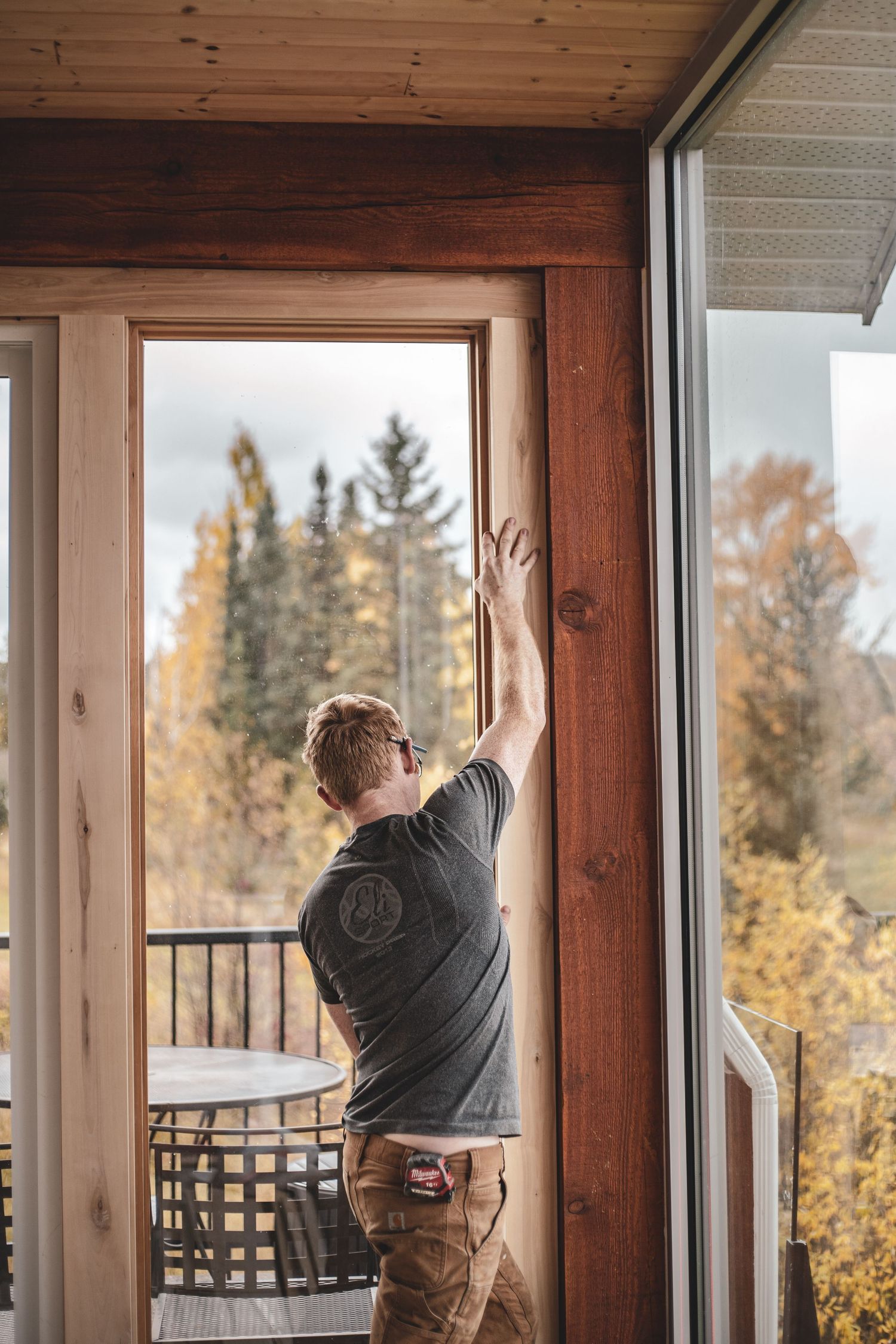 Craftsman installing a wooden door frame with autumn forest view visible through glass panels during Commercial Business Branding photoshoot