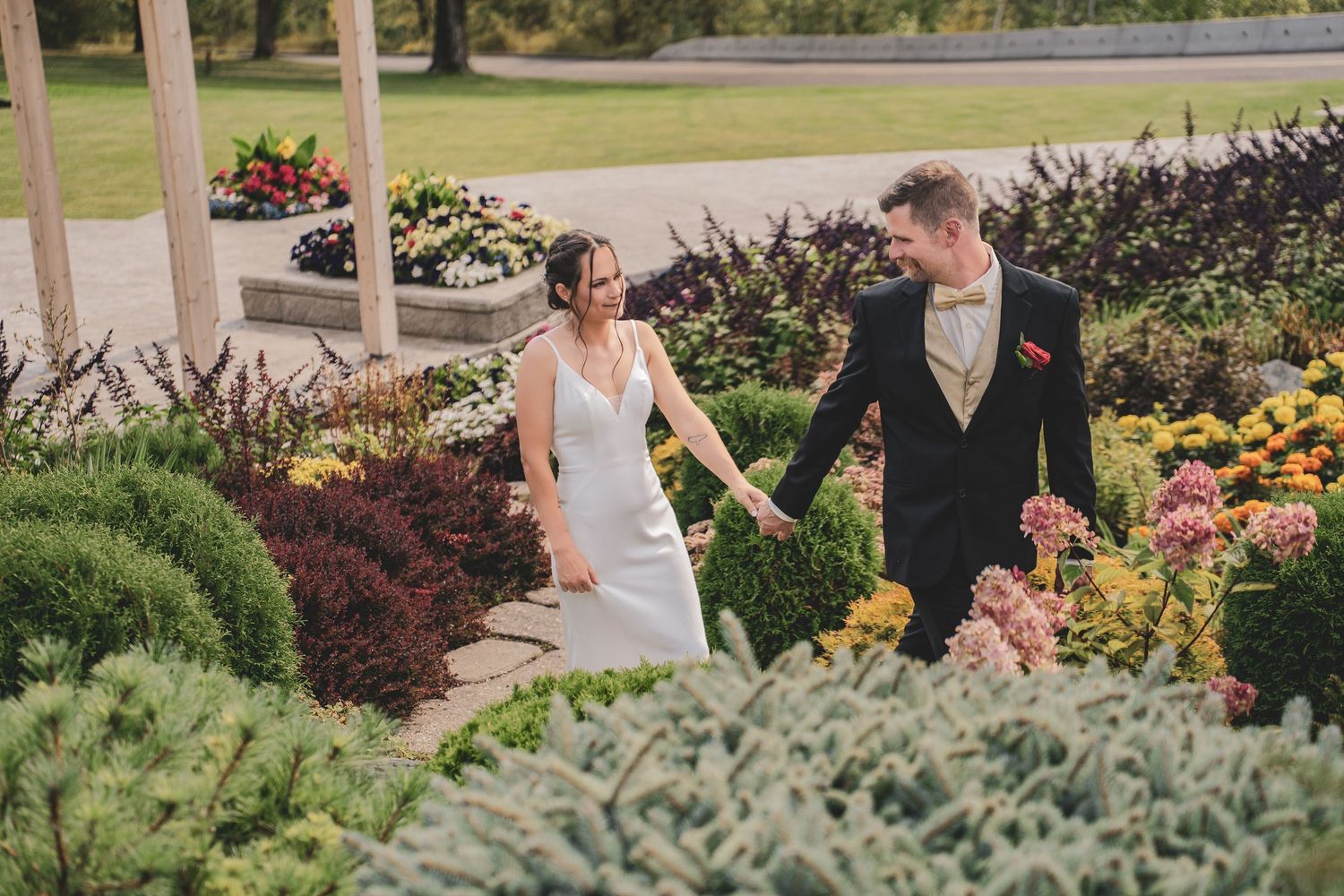 Bride and groom walking hand in hand through lush garden pathway on wedding day.