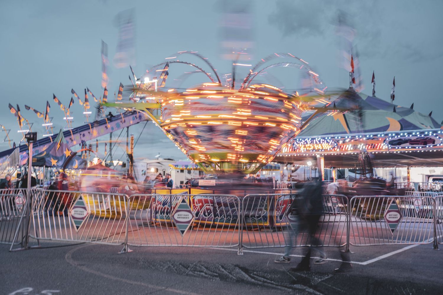 Long exposure shot of spinning carnival ride with colorful lights at twilight fairground.
