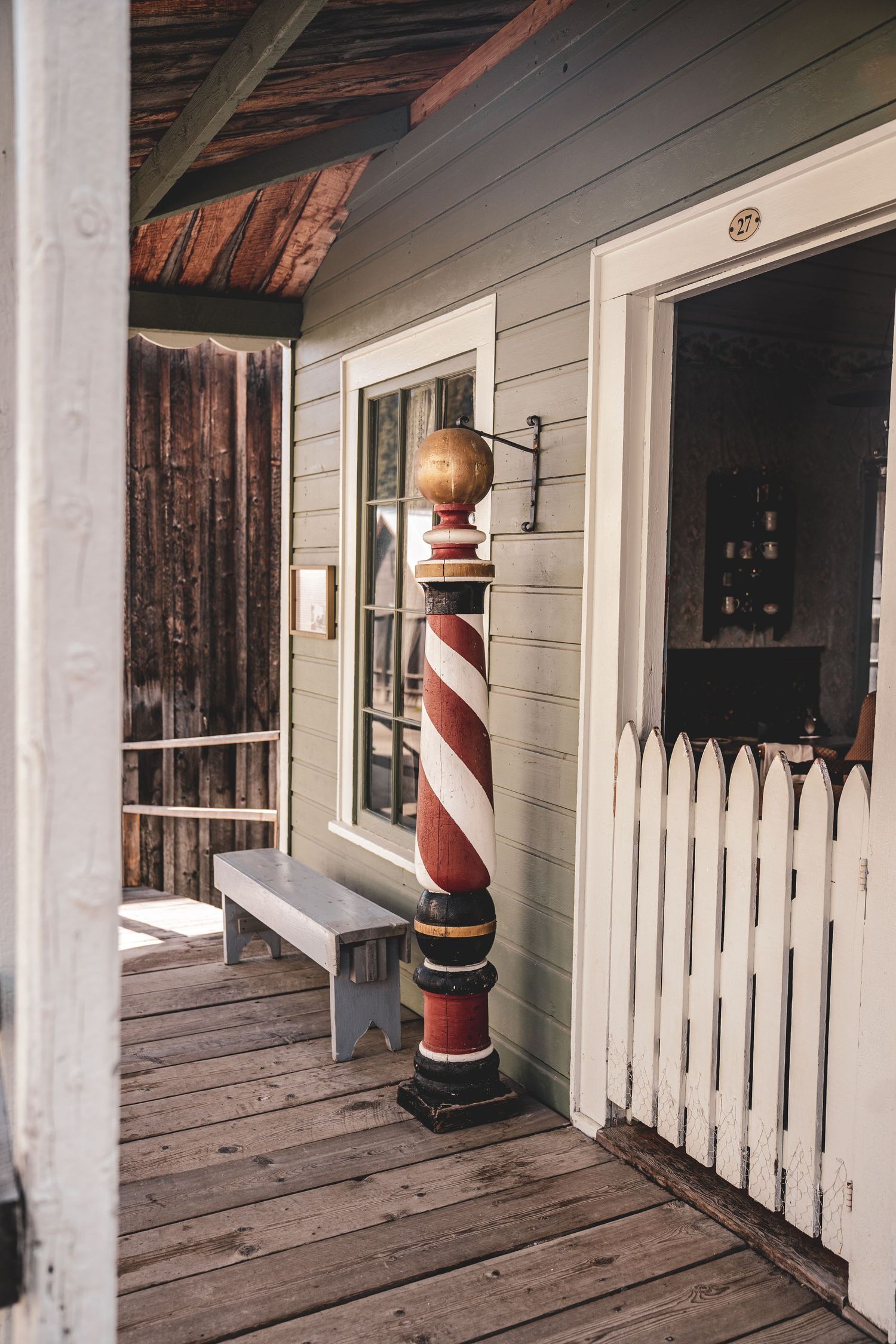 Classic red and white barber pole outside a rustic wooden building with a white picket fence.