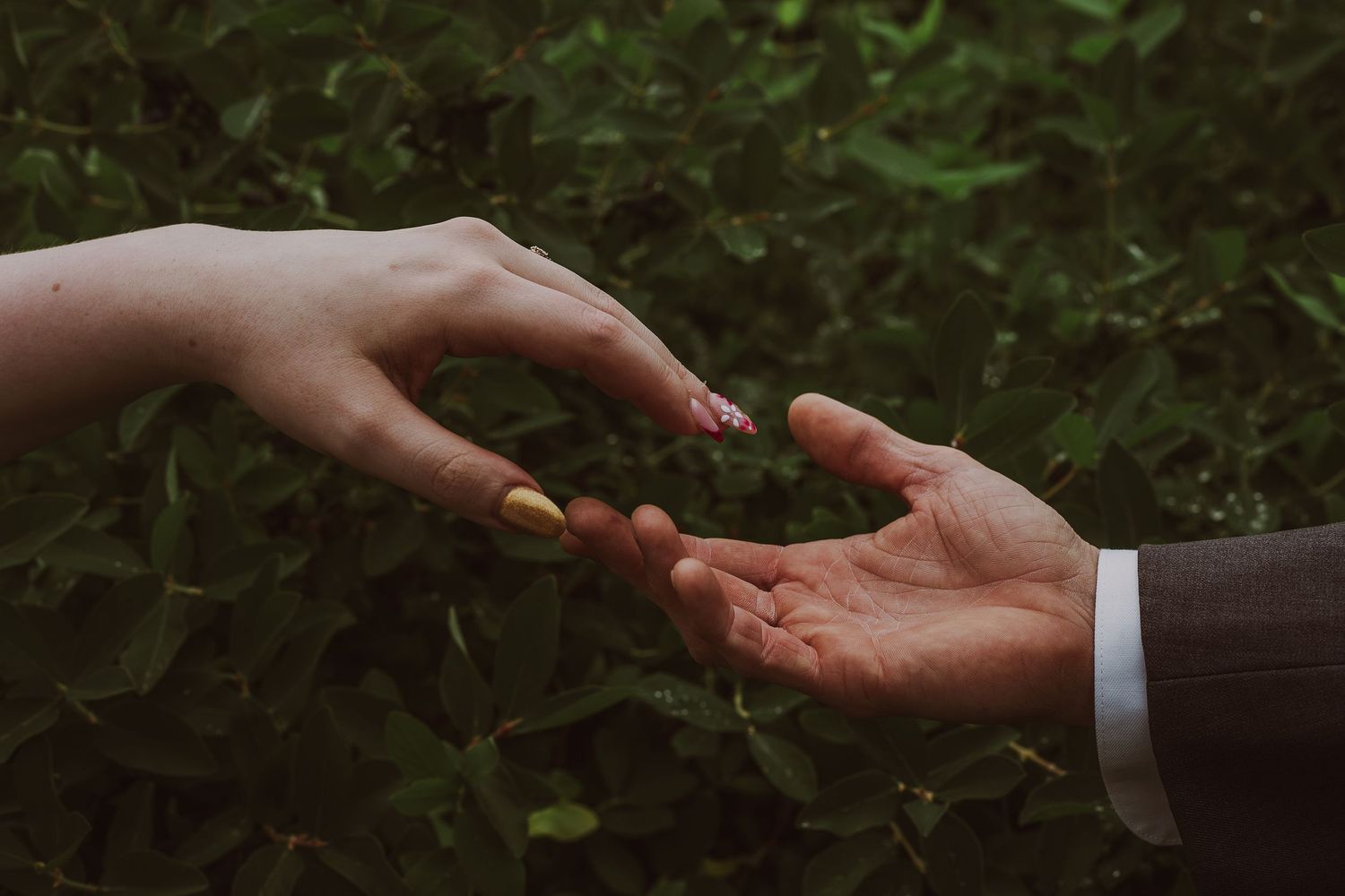 Artistic Photography of bride and groom gently touching hands against lush green foliage background. Wedding Photoshoot.