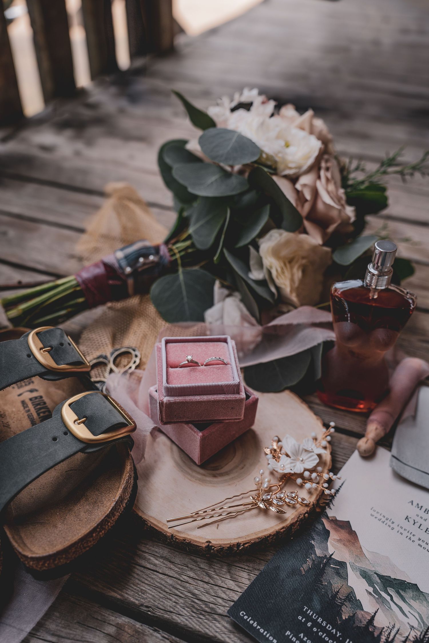 Wedding flat lay with floral bouquet, engagement ring, sandals, and accessories on wood.