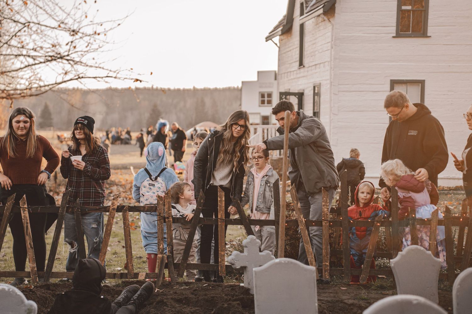 Families gather outdoors near a historic white farmhouse for a community event on a crisp autumn day at the huble homestead halloween event.