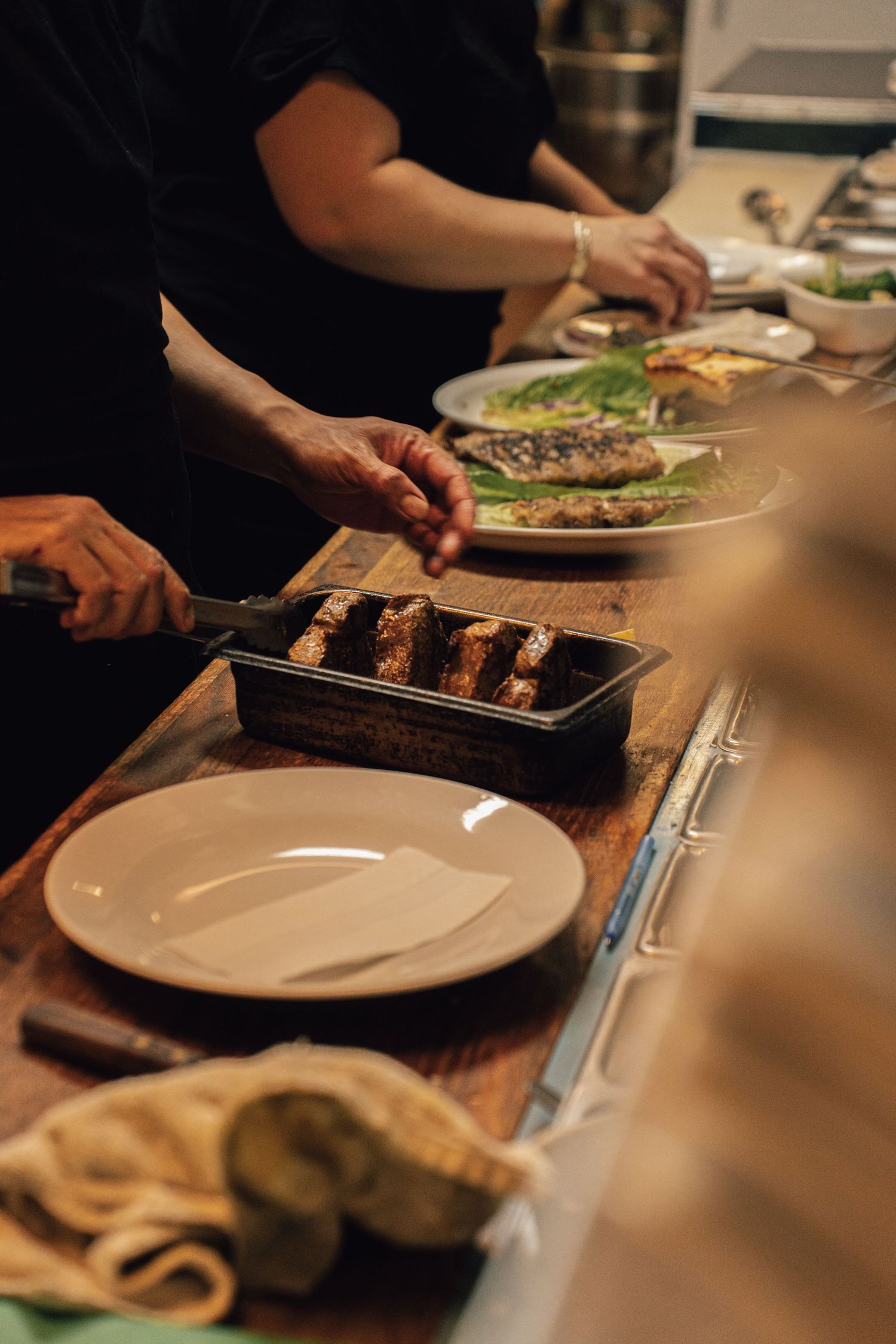 Chef plating grilled meat skewers in a restaurant kitchen with fresh fish and bread nearby.