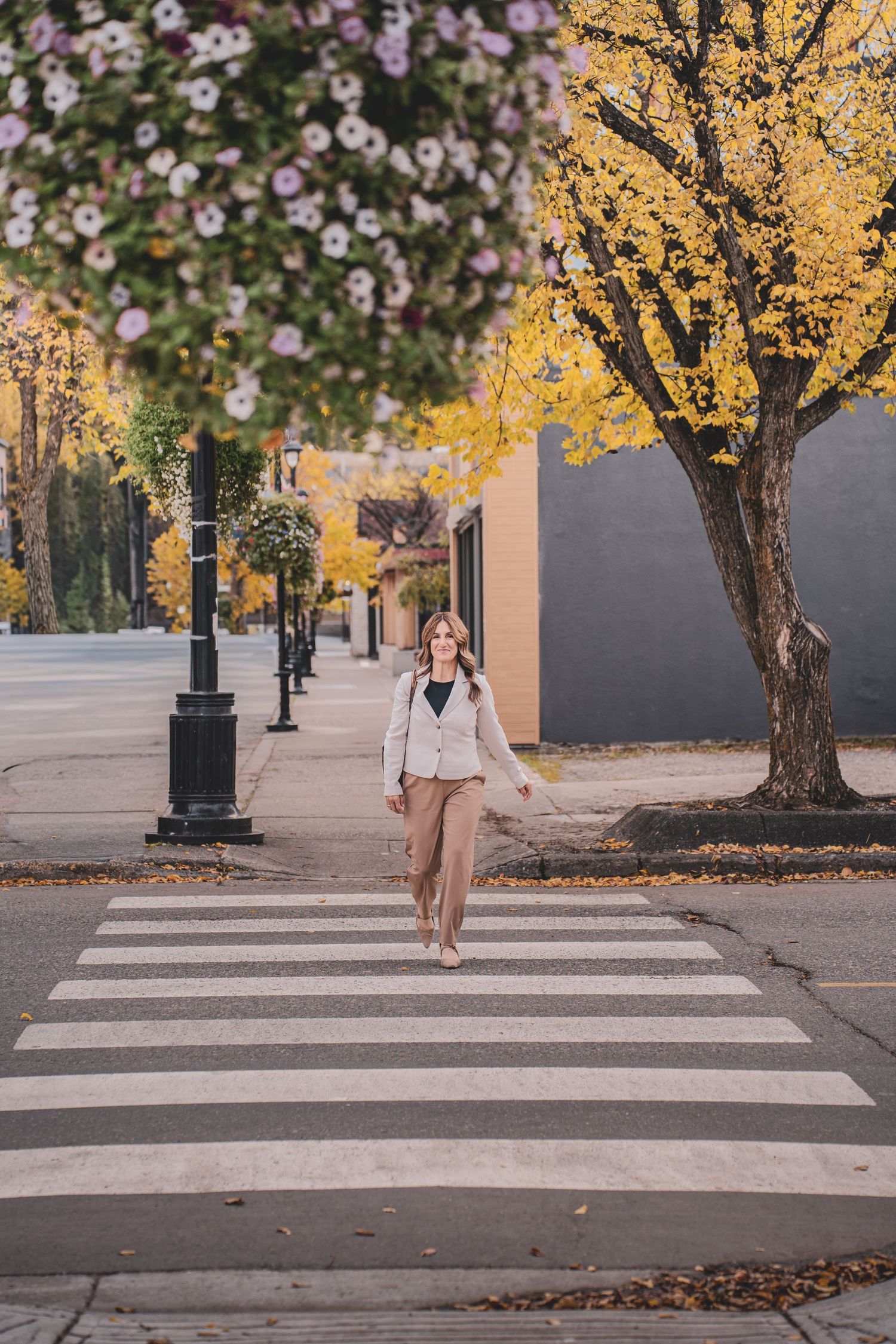 Businesswoman crossing a street crosswalk surrounded by vibrant autumn trees.