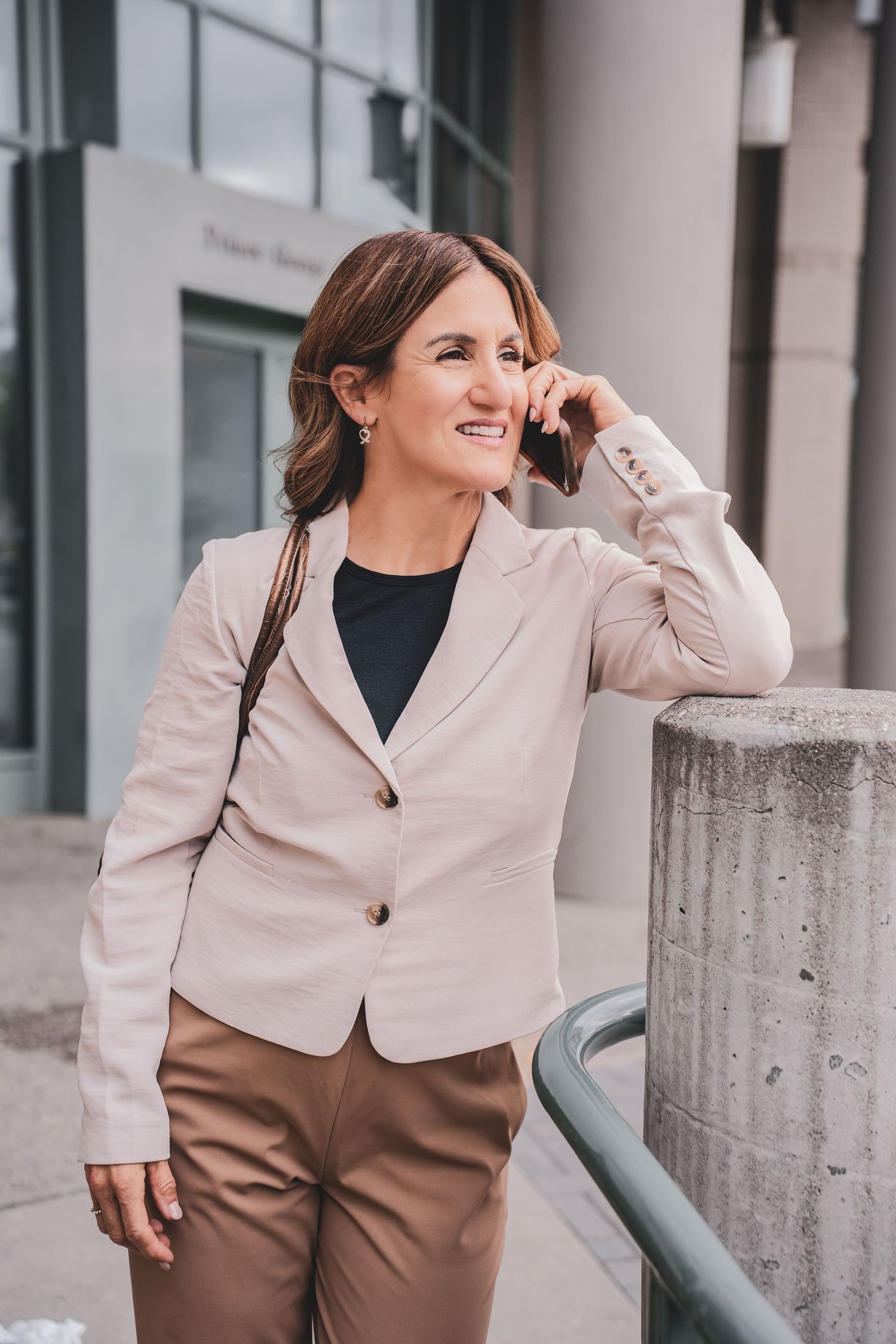 Professional  headshot photography of a woman in beige blazer smiling while talking on phone outdoors near the courthouse Prince George, BC