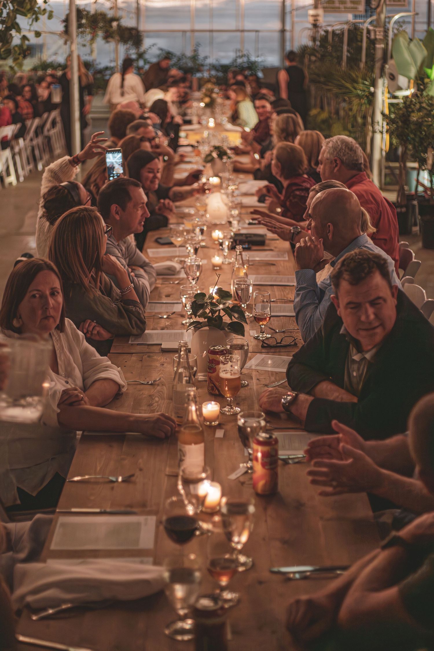 A long candlelit dinner table filled with guests enjoying an elegant evening event inside the Art Knapps greenhouse Prince George tourism.