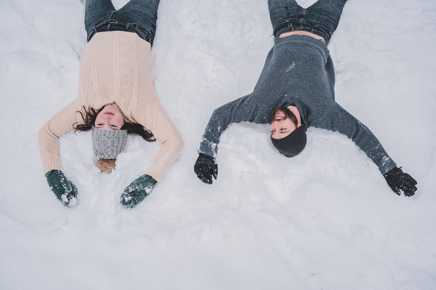 Happy couple lying on their backs in fresh white snow making snow angels outdoors.