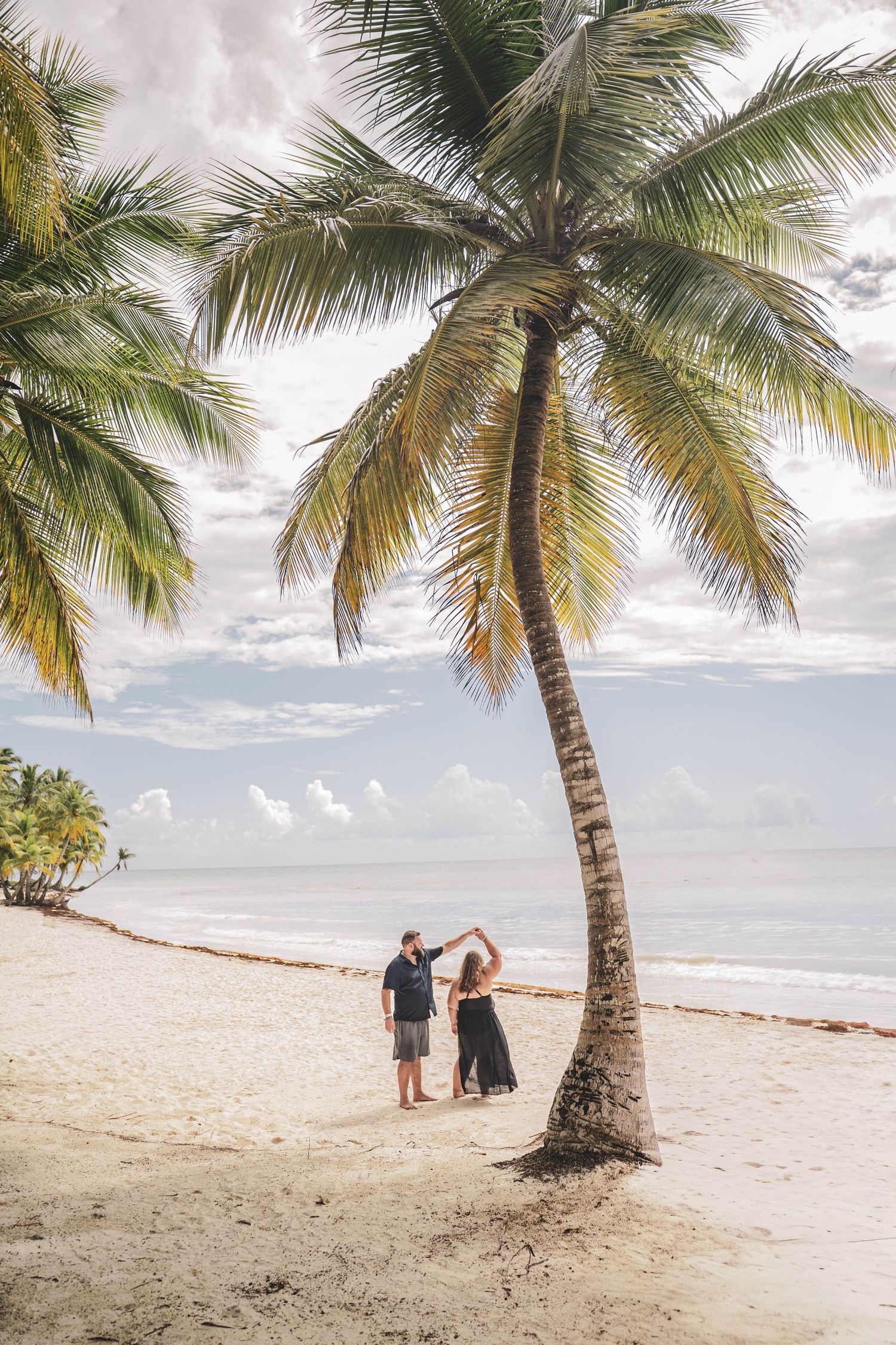 Couple dancing together under a tall palm tree on a tropical sandy beach with ocean views. Saona island. Dominican republic.