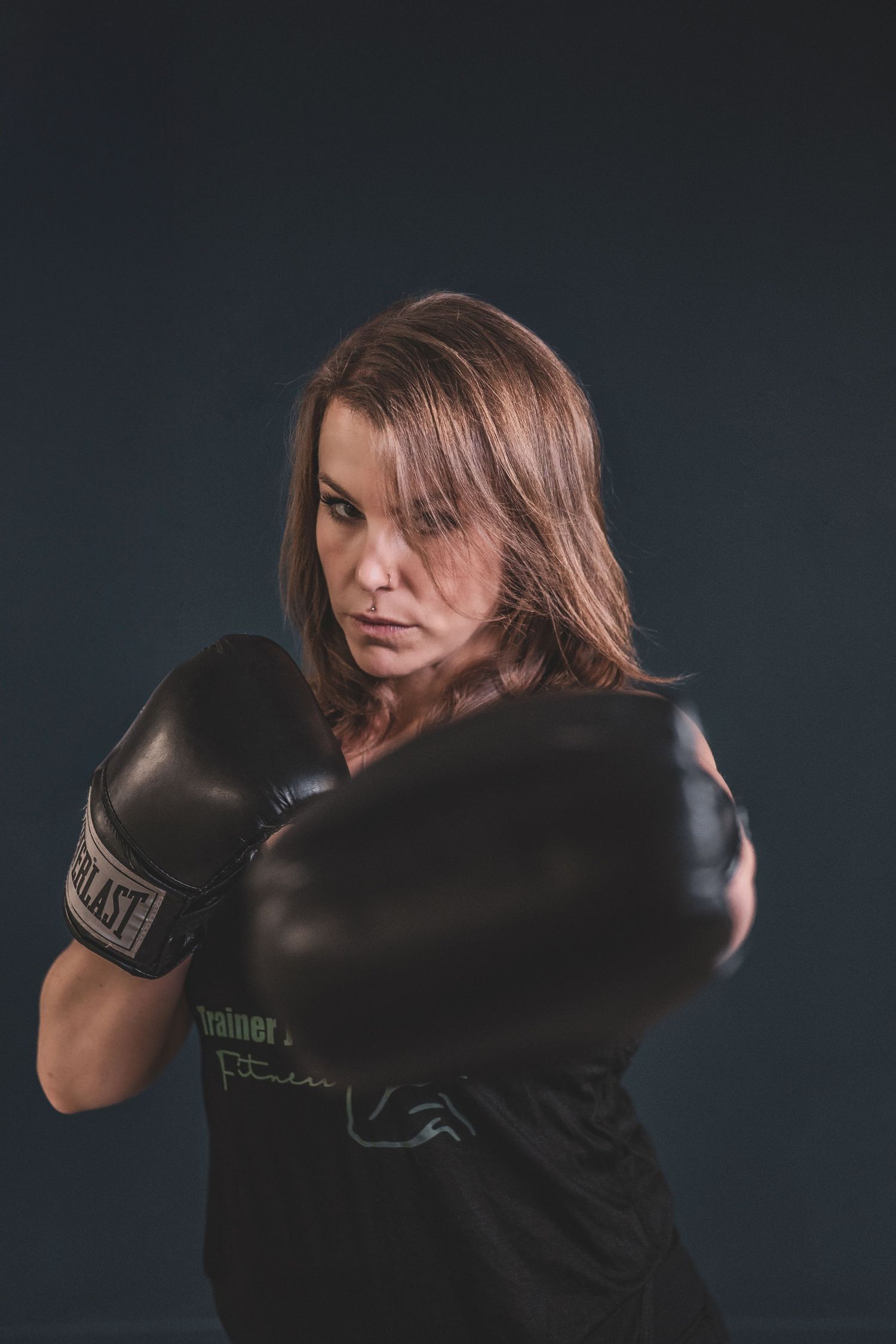 A determined woman in boxing gloves throws a punch toward the camera against a dark background during a branding photoshoot.