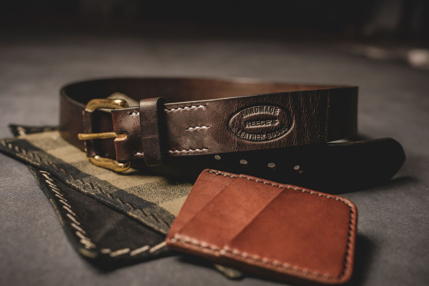 Product photography of Handmade dark brown leather belt with brass buckle beside slim tan leather card wallet.