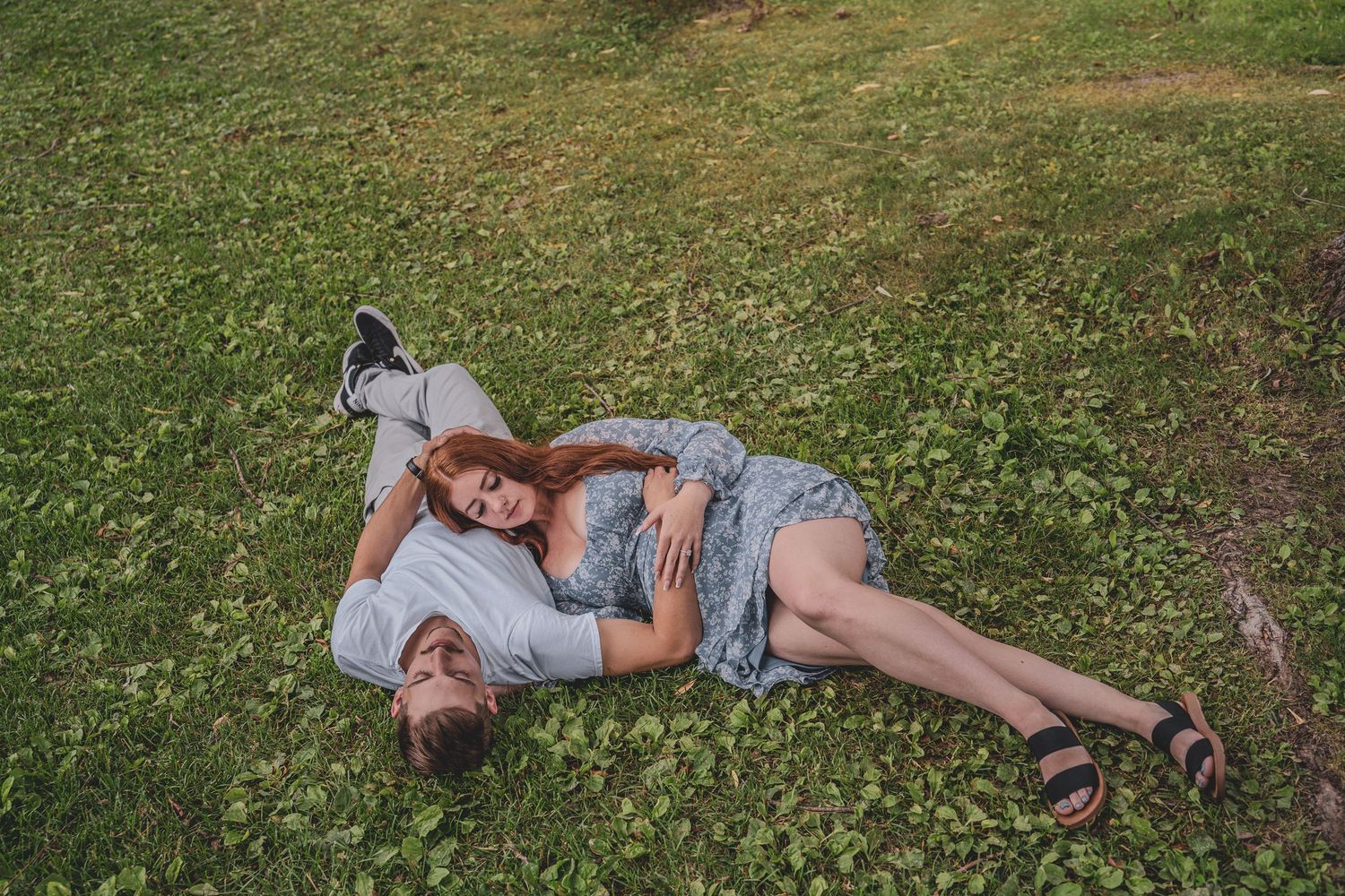Couple lying together on lush green grass in a playful and romantic outdoor engagement session.
