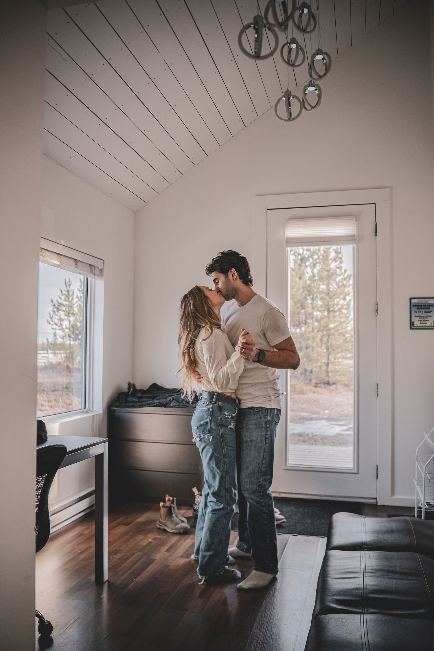 Couple shares a tender kiss in a modern living room with vaulted ceilings and large windows at woodhouse ranch and suites in PG.
