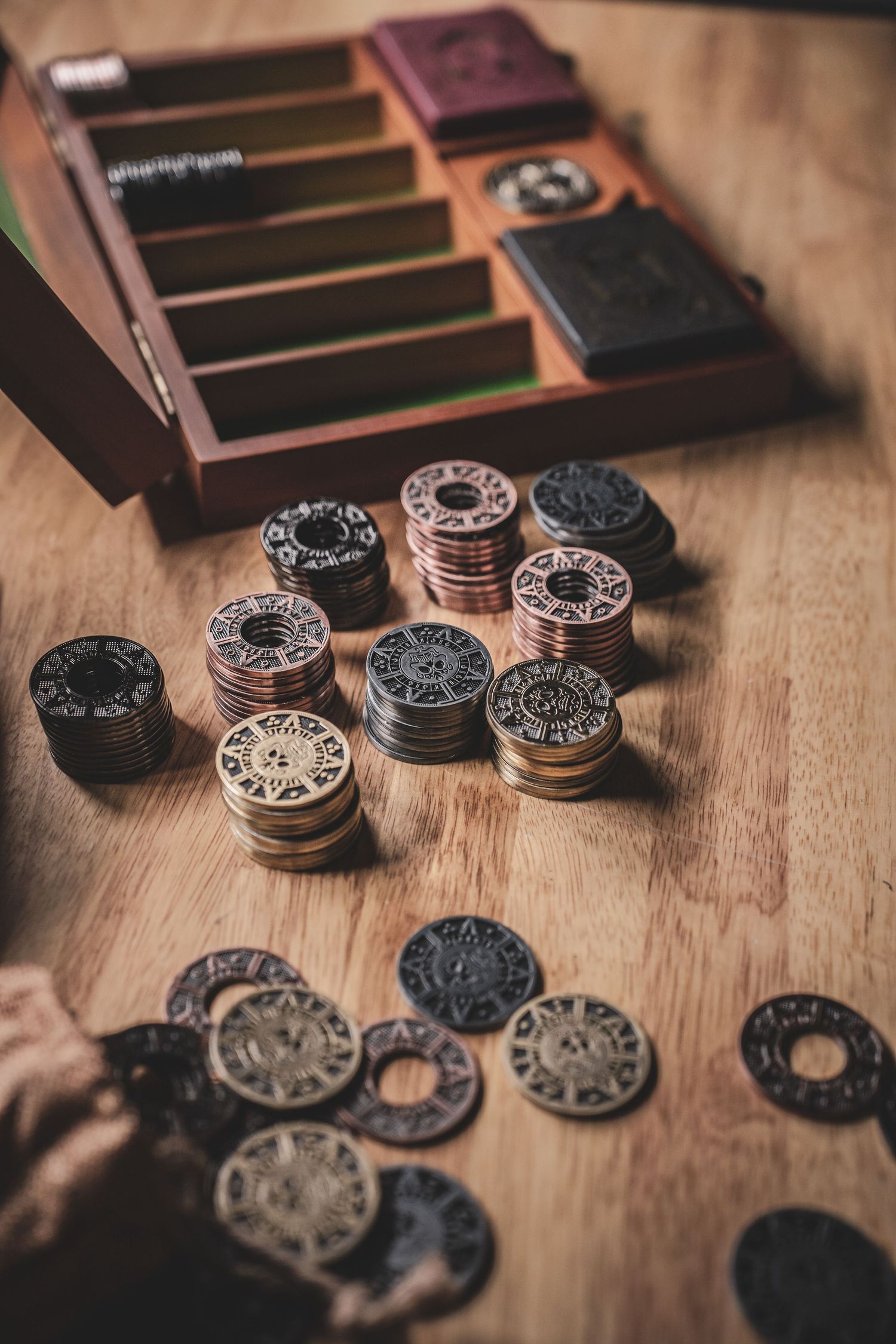 Stacks of ornate bronze and copper coins beside wooden storage box on table.