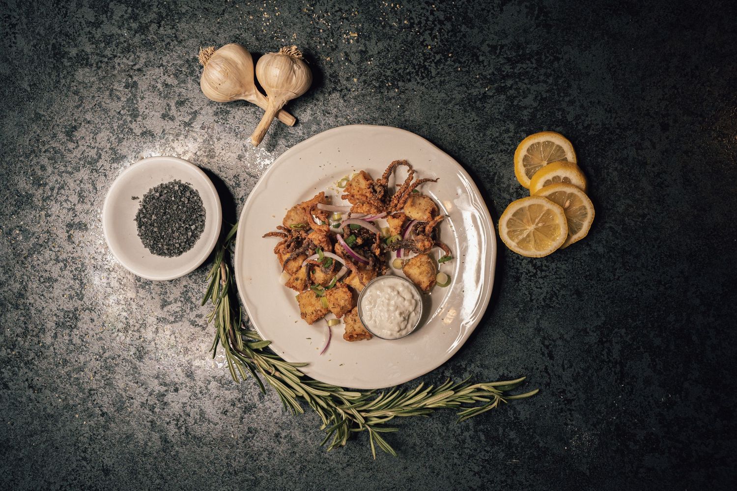 Grilled calamari and shrimp on a white plate with garlic, rosemary, lemon, and dipping sauce.