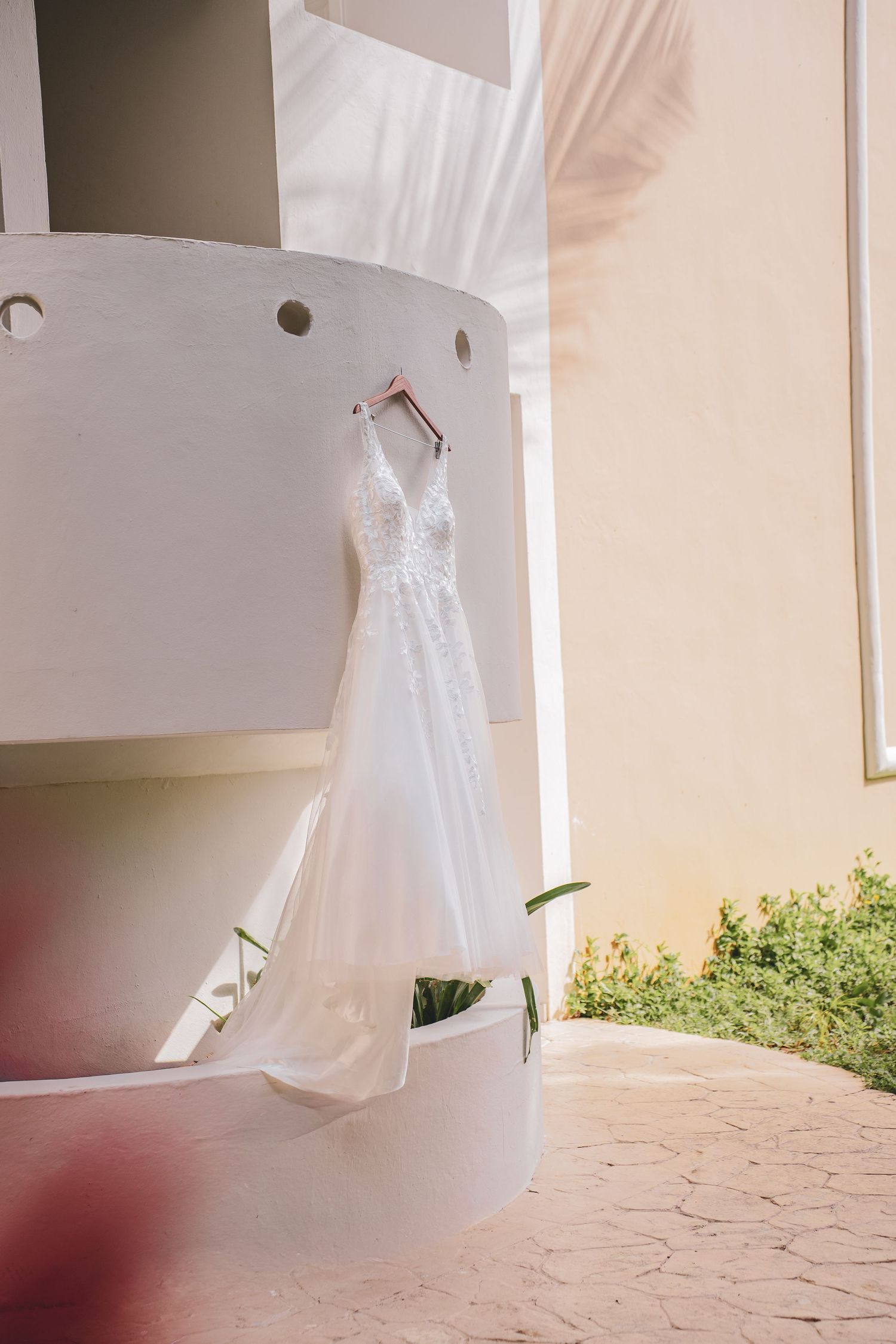 Elegant white lace wedding dress hanging on a hanger at a bright outdoor tropical elopement, offered by Free West Photography.