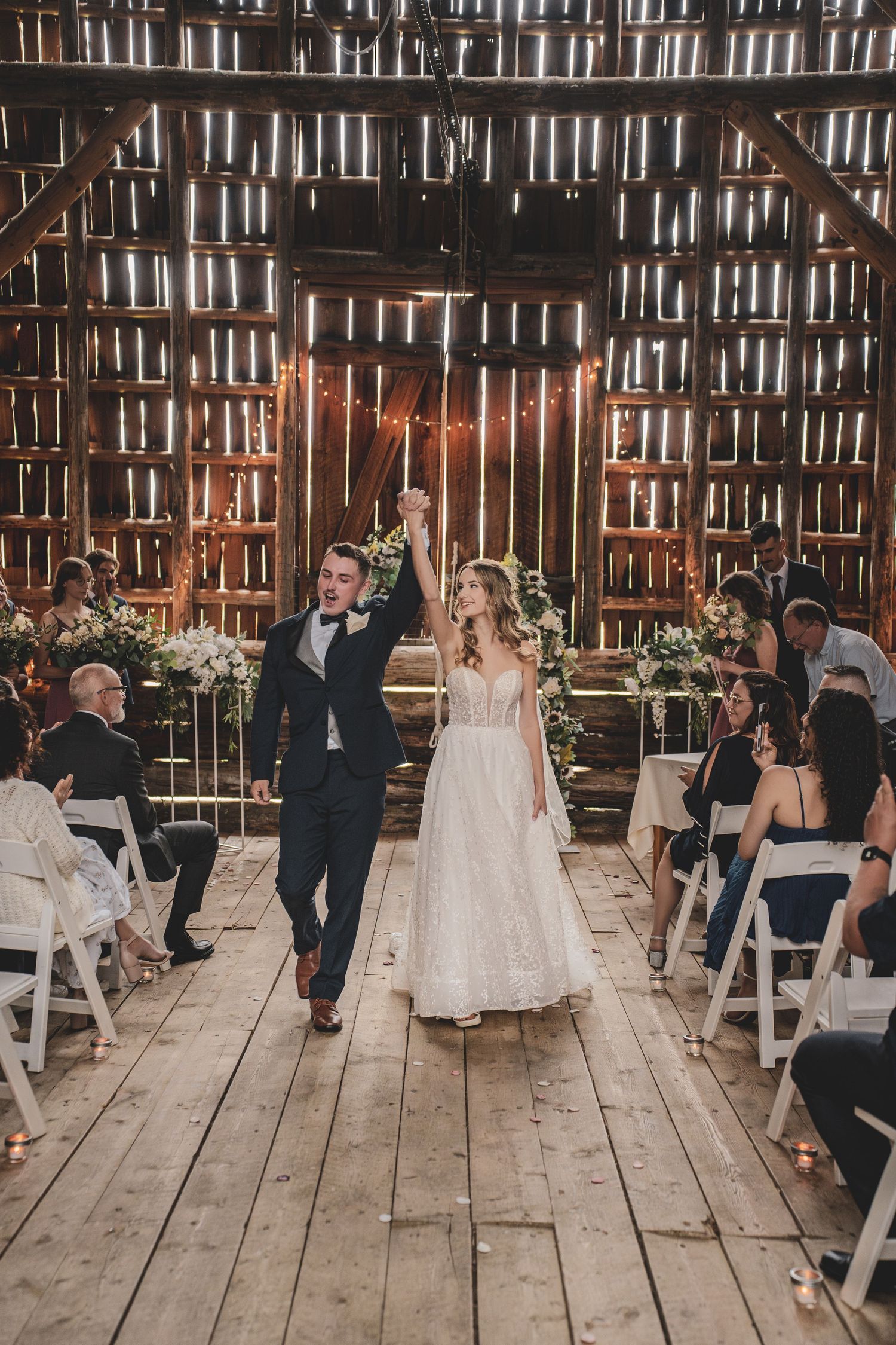 Newlyweds celebrate their recessional in a warmly lit rustic barn wedding venue with string lights at huble homesrtead wedding venue.