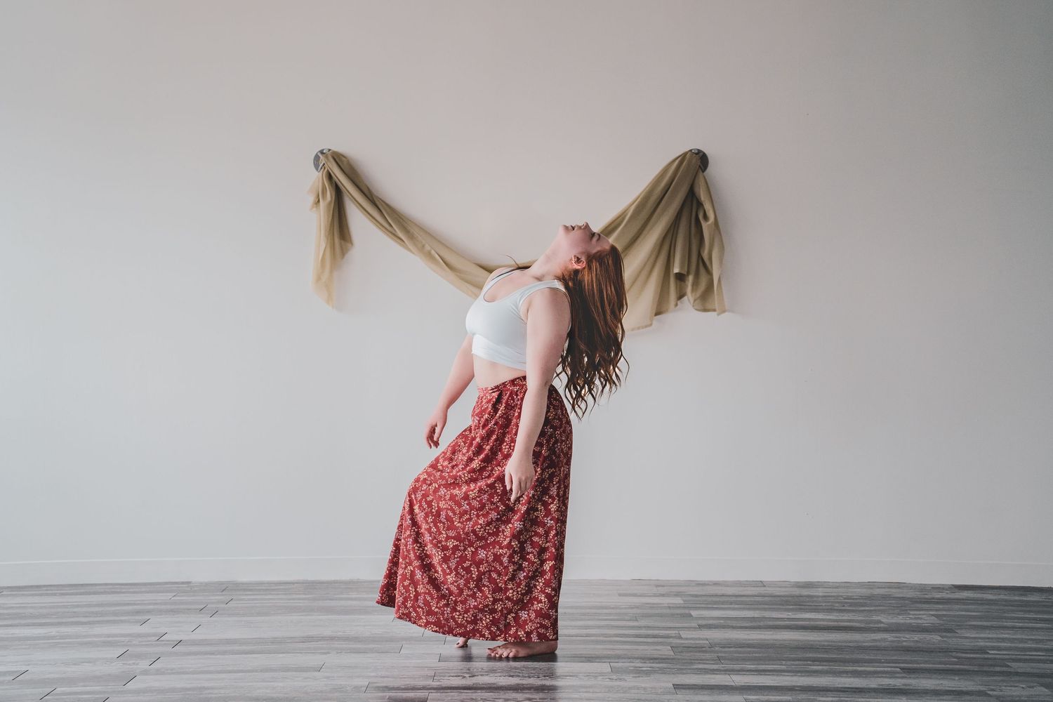A woman in a white top and floral maxi skirt poses dramatically with fabric flowing behind her indoors during a commercial photoshoots.
