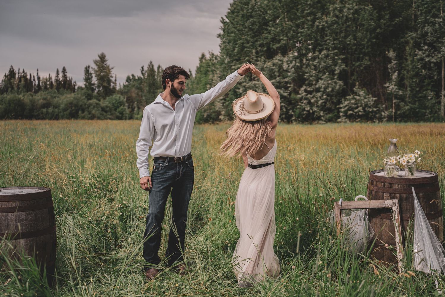 Prince George Couple dancing in a rustic outdoor field with wooden barrels and wildflowers during a country style elopement celebration.