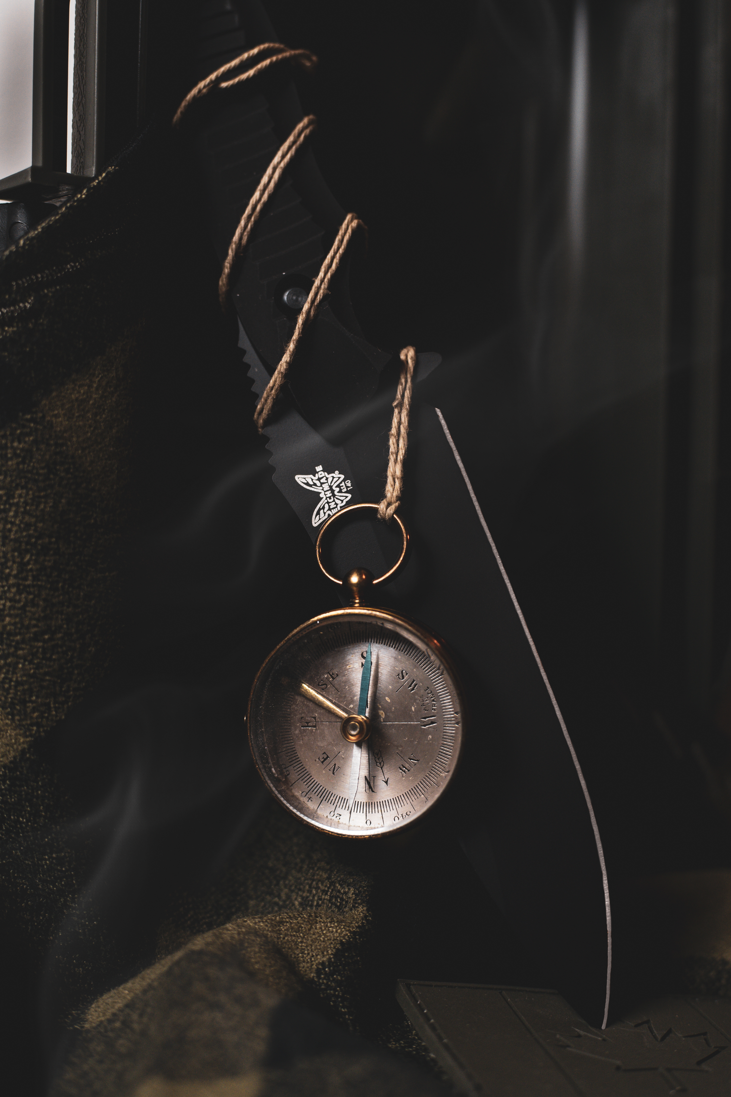Product photography of Vintage brass compass with butterfly charm hanging on twine rope against dark moody background.