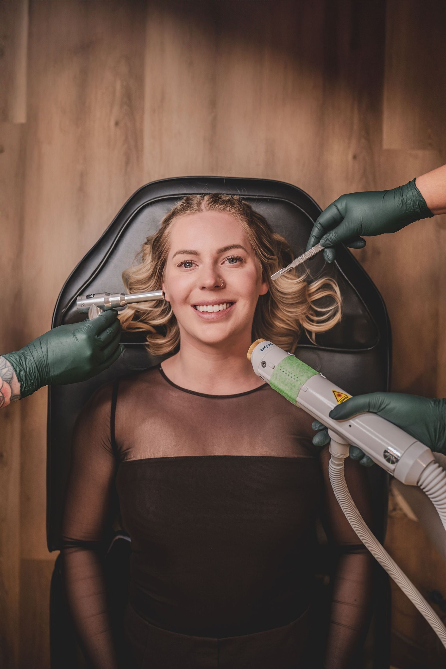Smiling woman receiving facial laser treatment in salon chair with gloved hands holding beauty devices. Business Photography of Luxe PG