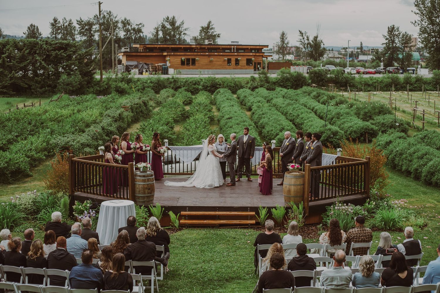 Outdoor wedding ceremony on a wooden deck surrounded by lush green lavender fields and guests at Northern Lights Winery, Prince George, BC.