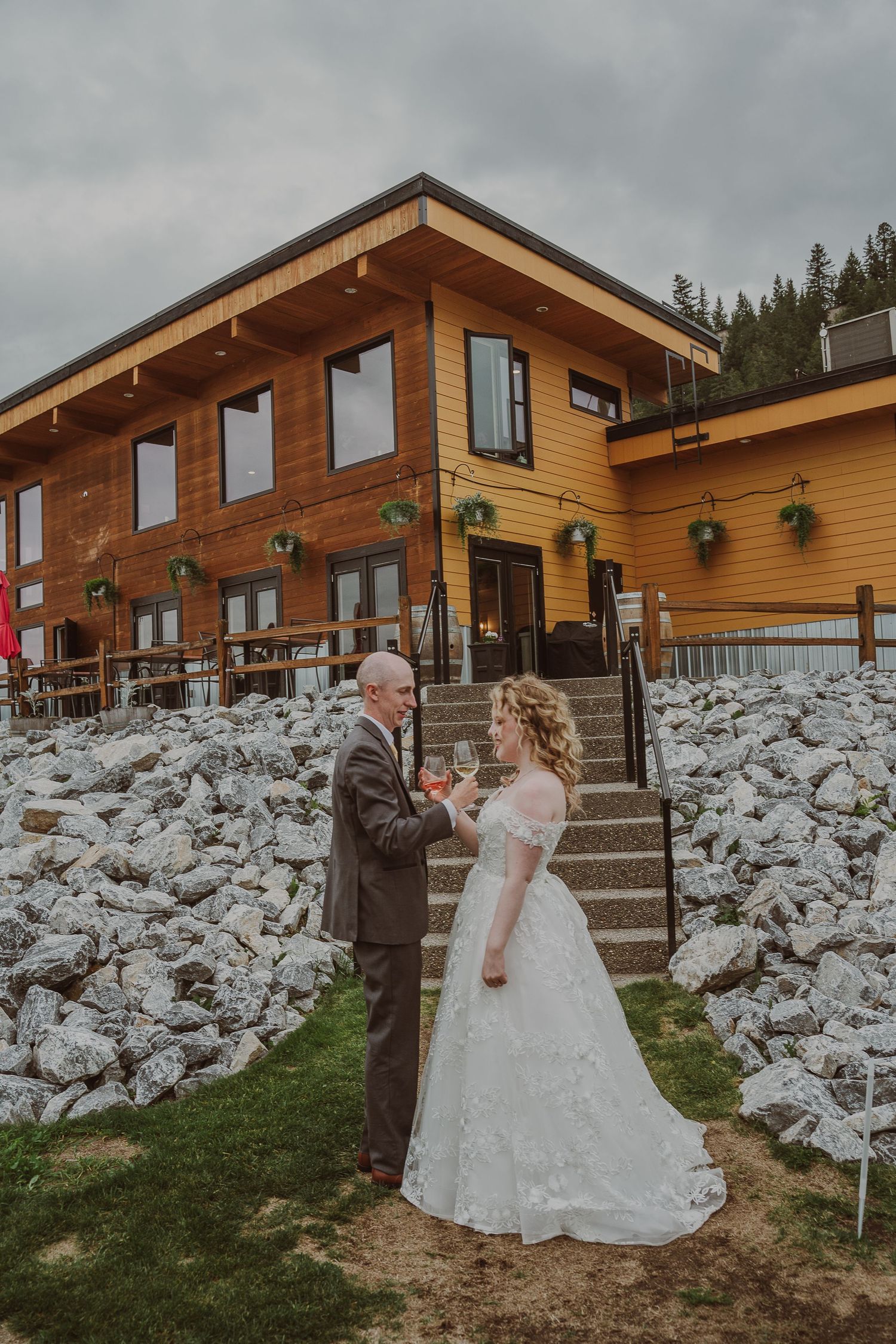 Bride and groom holding hands in front of rustic wooden wedding venue with rock landscaping during their wedding photoshoot in Northern BC.