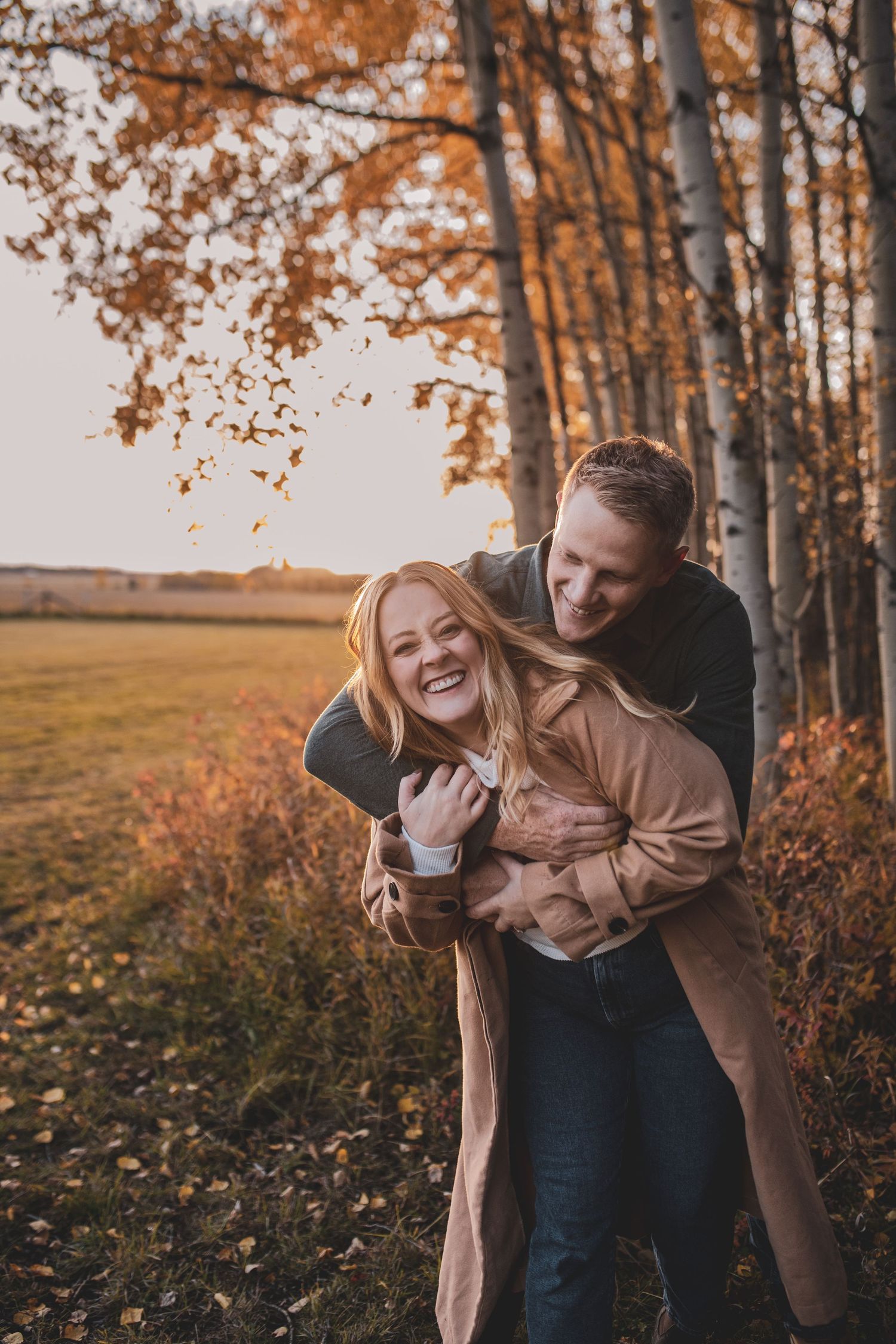 Happy couple embracing and laughing in a golden autumn forest during a romantic outdoor photo session.