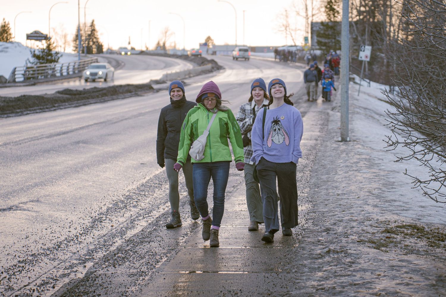 Four people walking together along a wet sidewalk on a cold winter day in a small town.