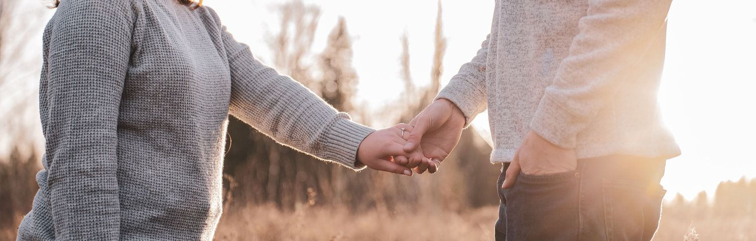 Couple holding hands tenderly in a golden sunlit field during a romantic outdoor engagement session.