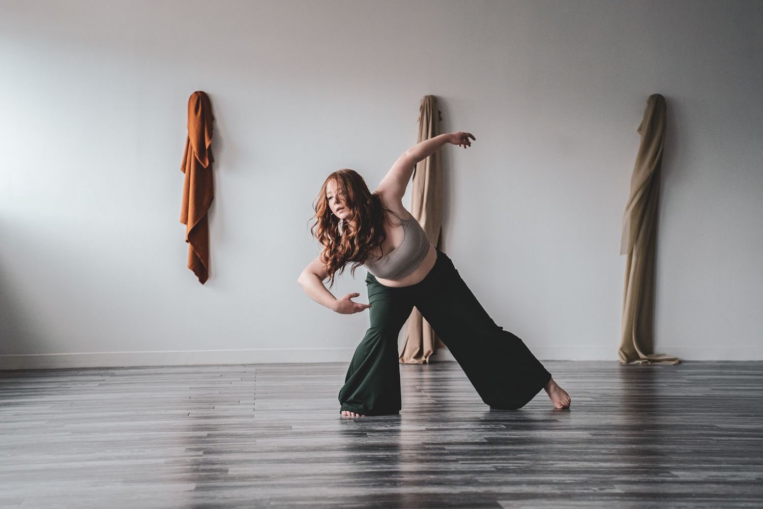 Pregnant woman dancing expressively in a minimalist studio with fabric wall hangings.