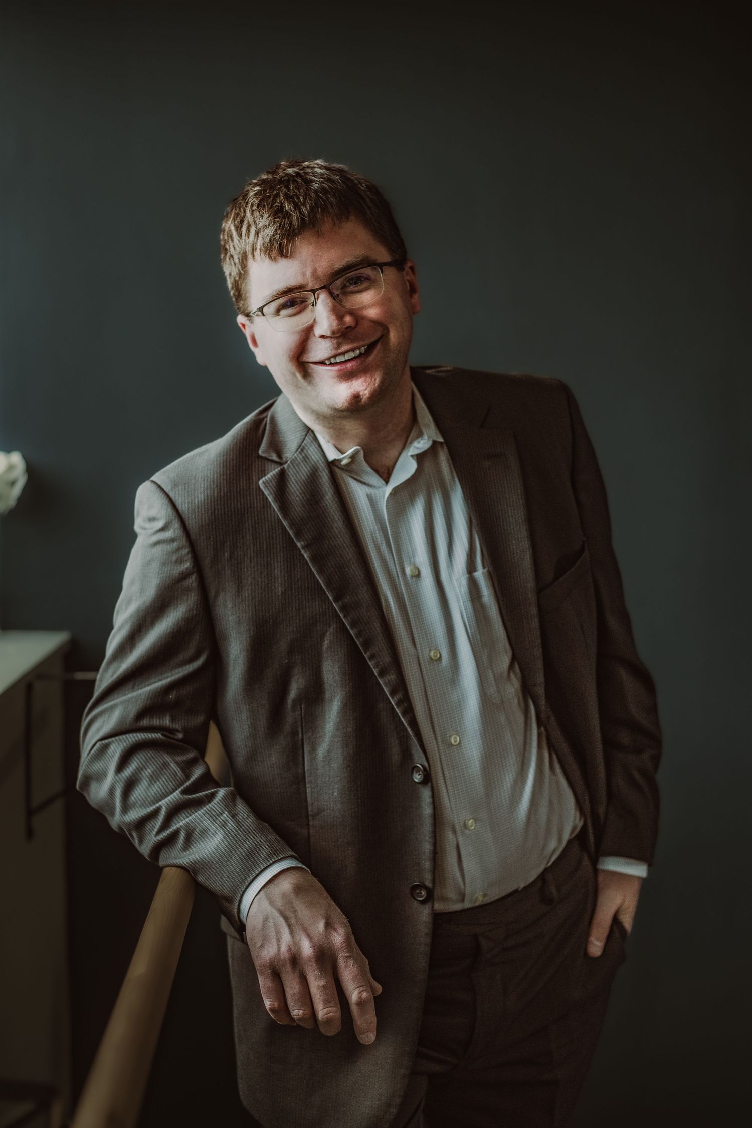 Cheerful man in gray blazer and glasses laughing in professional indoor portrait photography during headshot photoshoot.