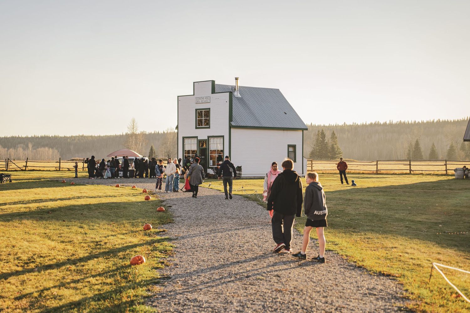 Guests walk along a gravel path toward a white farmhouse venue bathed in warm golden morning light at Huble Homestead's  Commercial Event.
