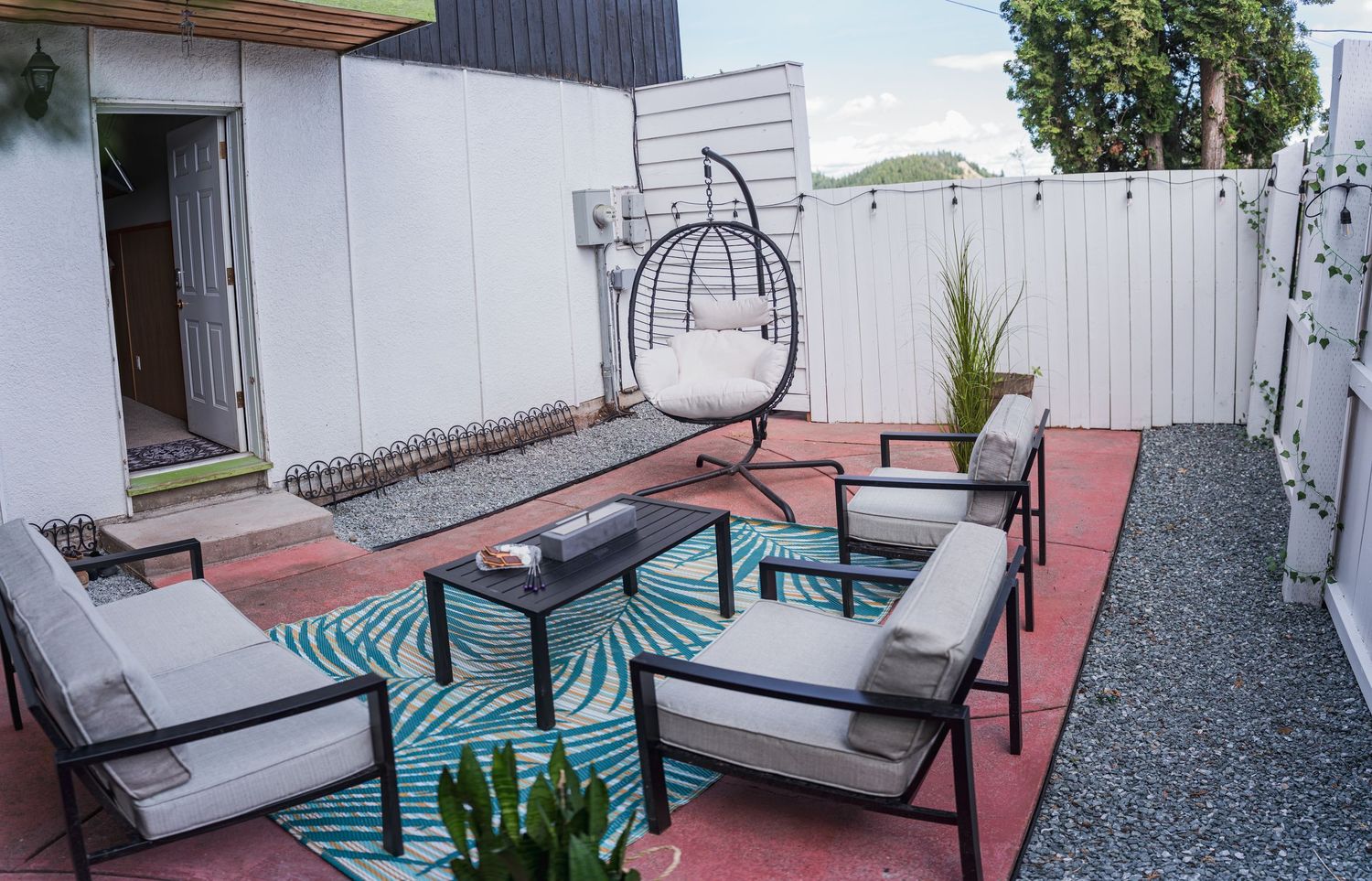 Modern outdoor patio with hanging egg chair, sectional seating, and tropical turquoise area rug.