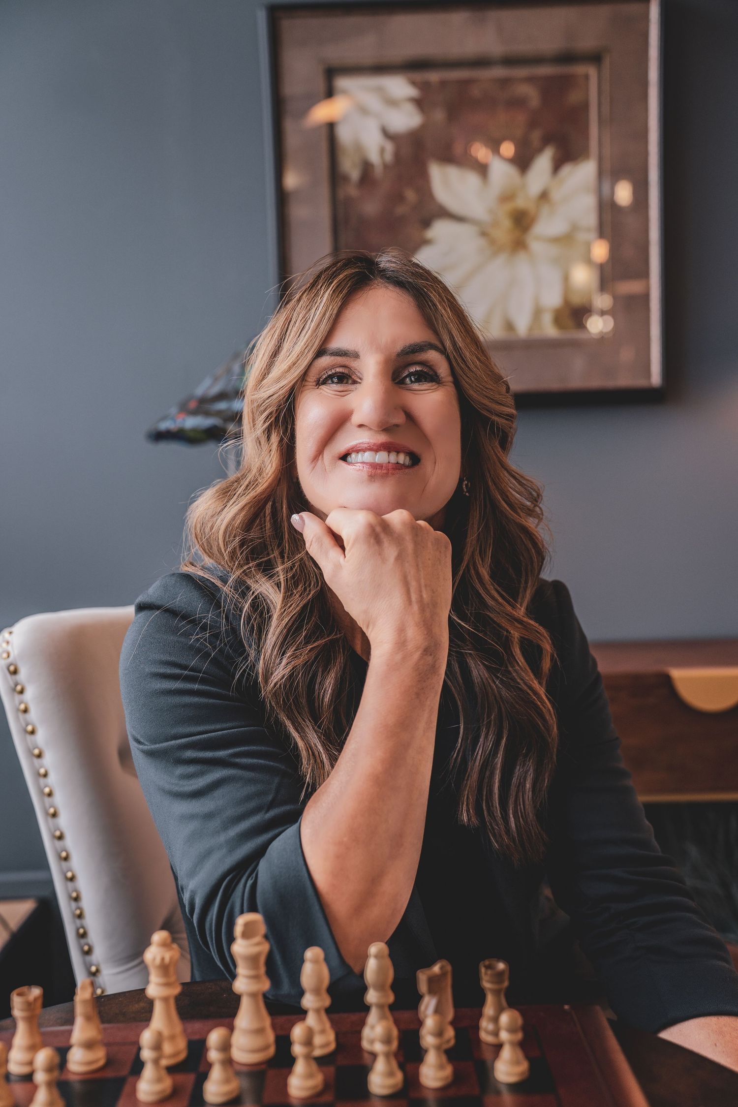 Smiling brunette businesswoman sitting at a chess board in a stylish office setting.