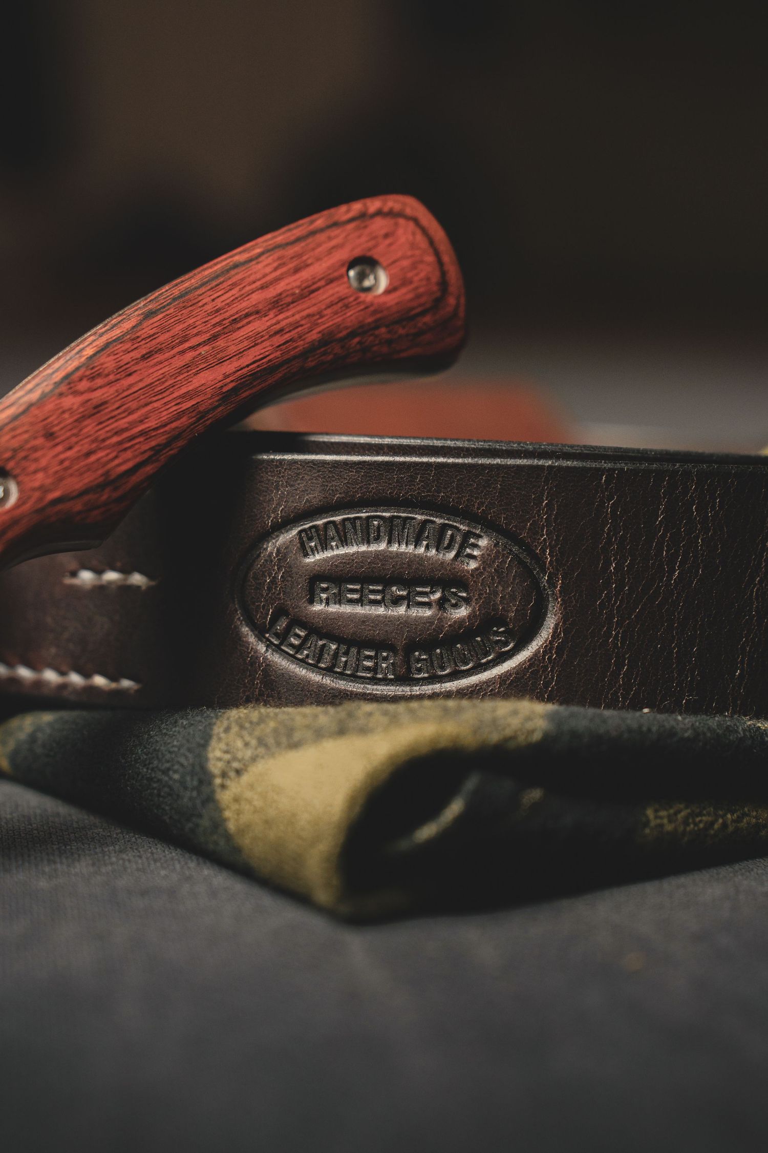 Product Photography of Reece's handmade leather goods embossed belt with wooden handle folding pocket knife on fabric.
