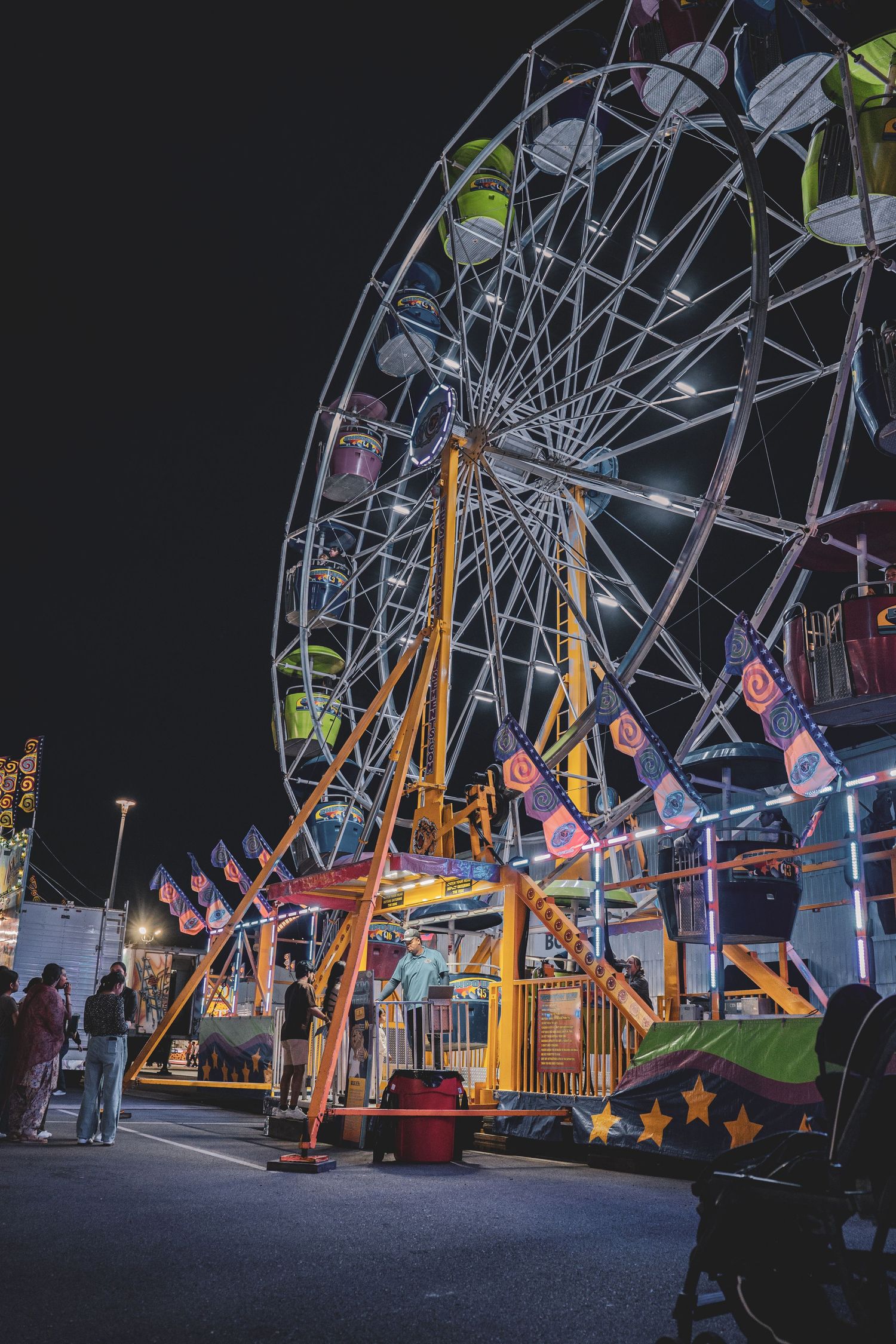 Illuminated Ferris wheel and carnival rides glowing against night sky at outdoor fairground.