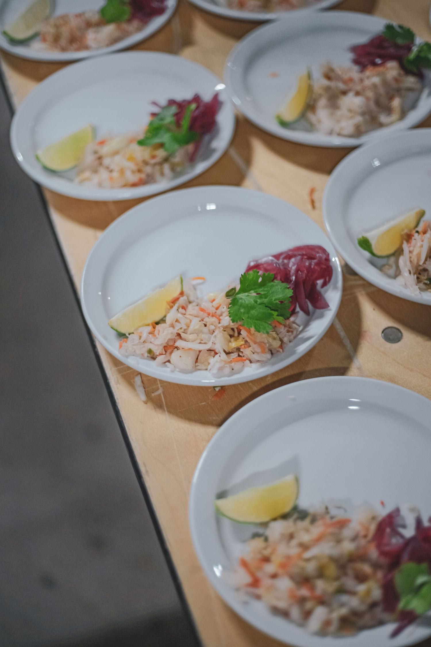 Multiple white plates of seafood salad garnished with lime and herbs arranged on a wooden surface.