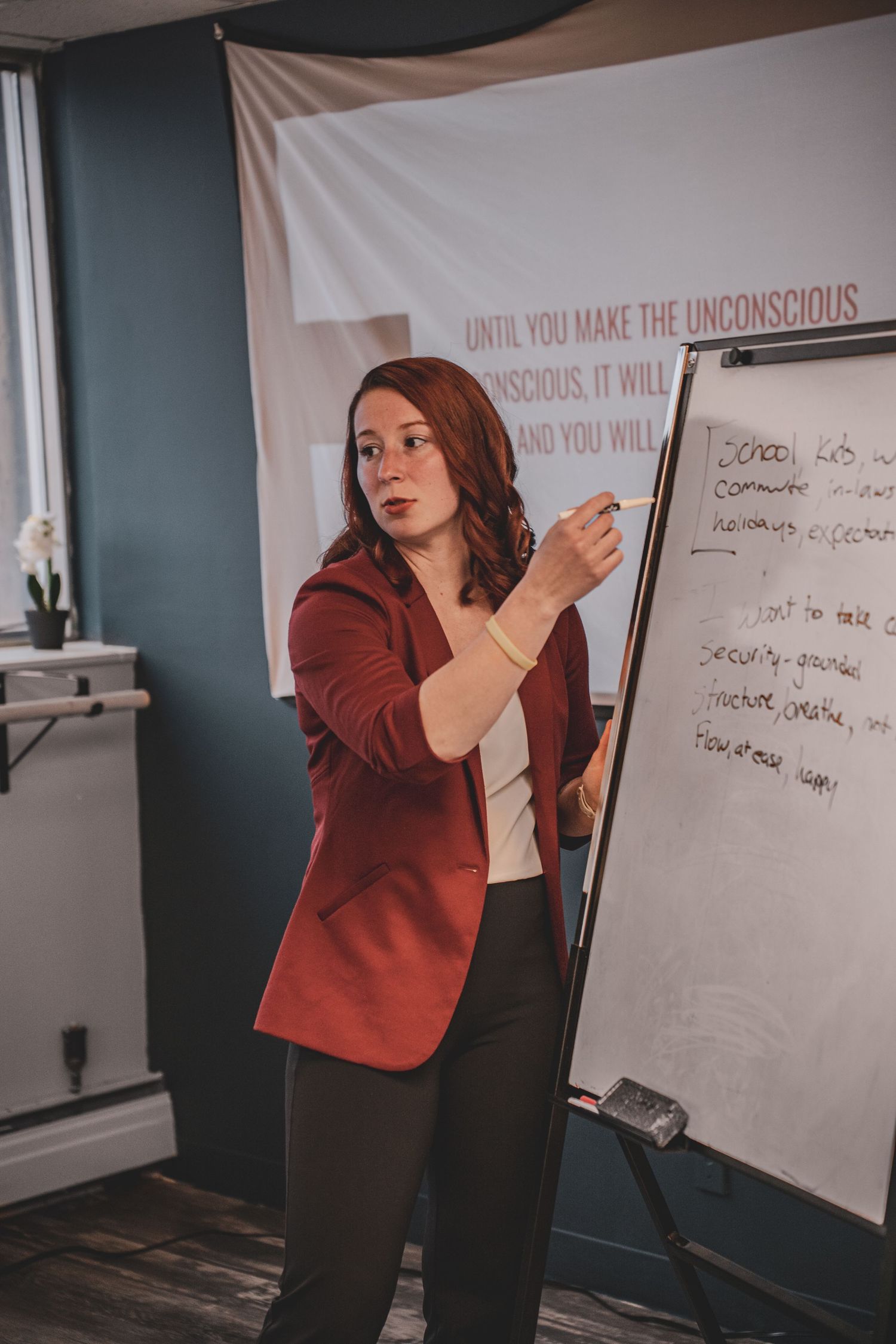motivational speaker in red blazer presenting at a whiteboard in a professional workshop setting during her commercial branding photoshoot.