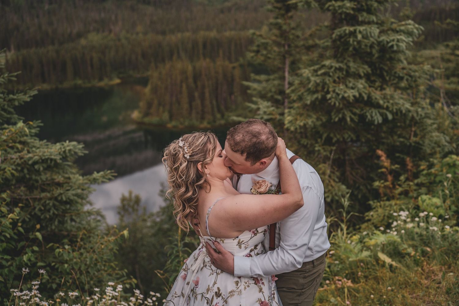 Couple sharing a passionate kiss on a mountain overlook surrounded by evergreen forest.