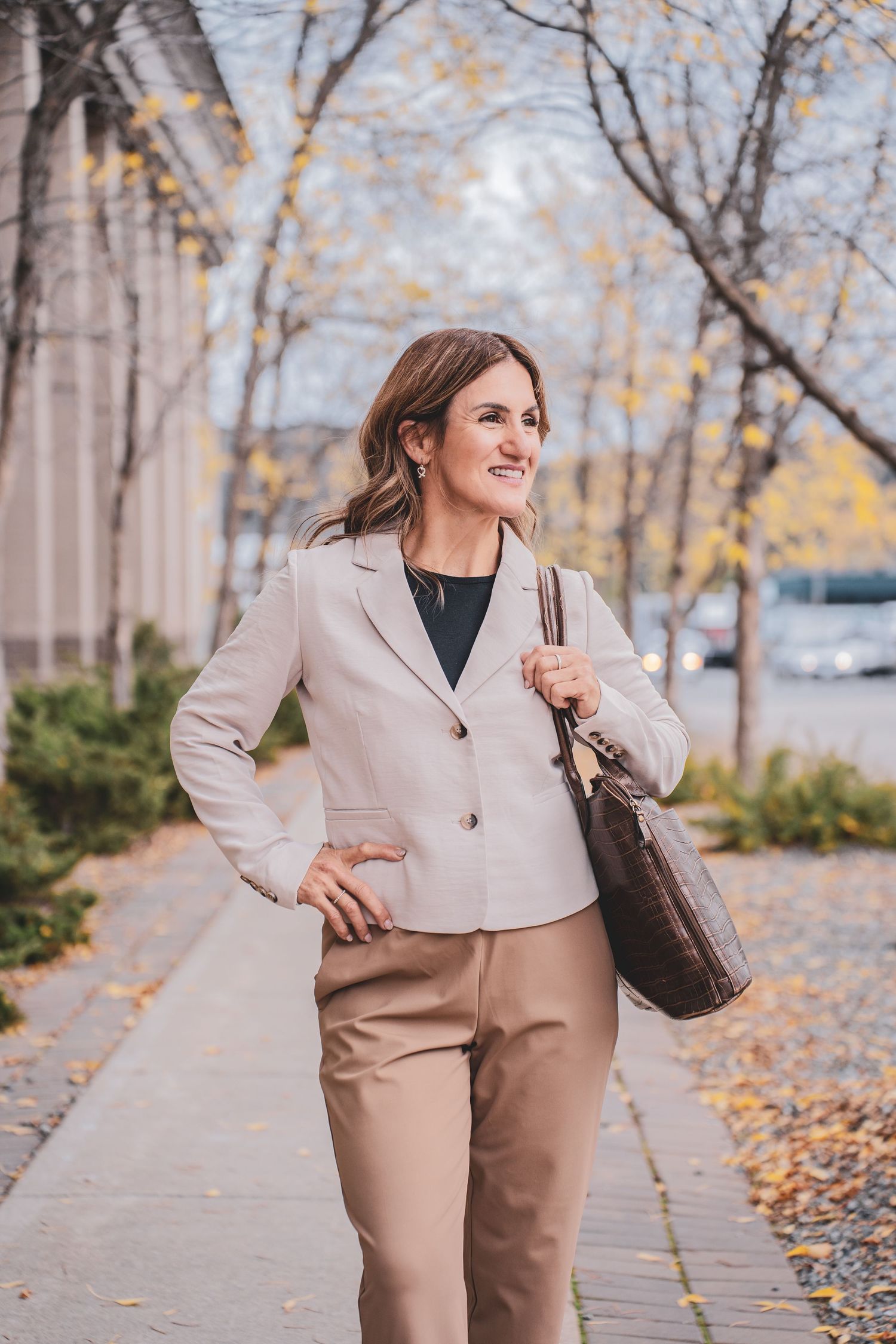 Stylish businesswoman walking outdoors in autumn carrying a brown leather tote bag.