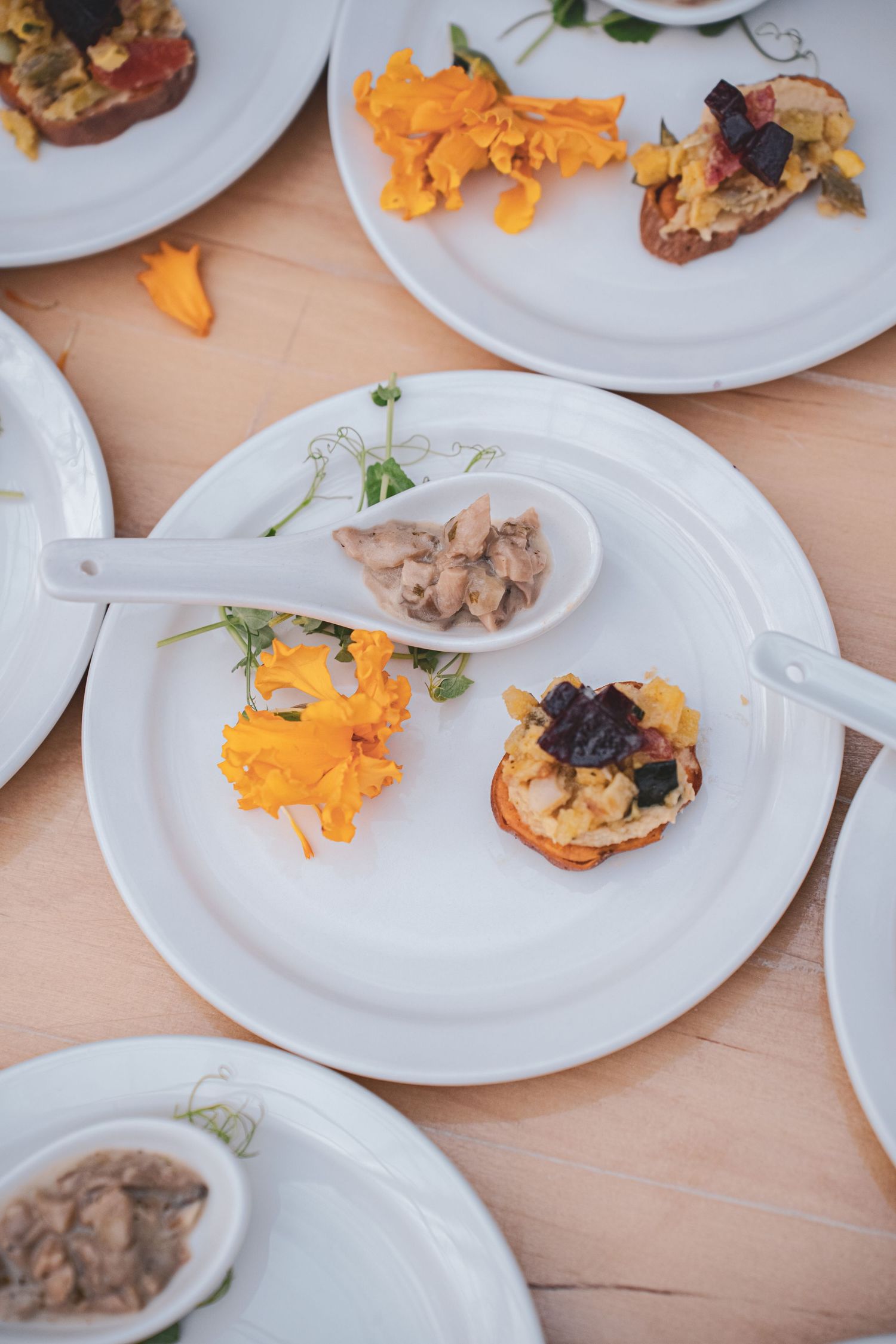 Elegant white plates with gourmet appetizers garnished with bright orange edible flowers on a wooden table.