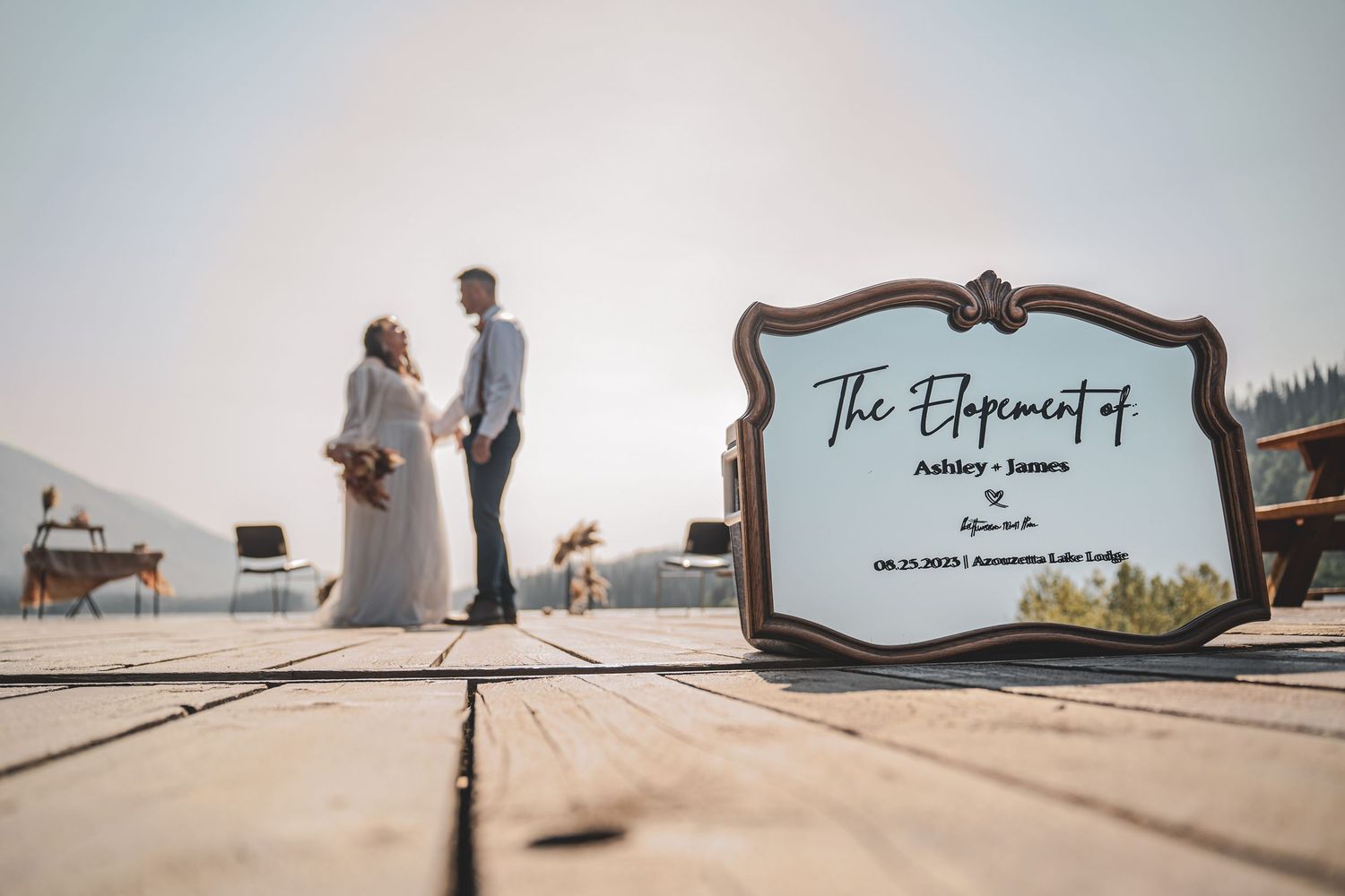 Elopement sign for Ashley and James displayed on dock with couple standing in background at mountain lake.