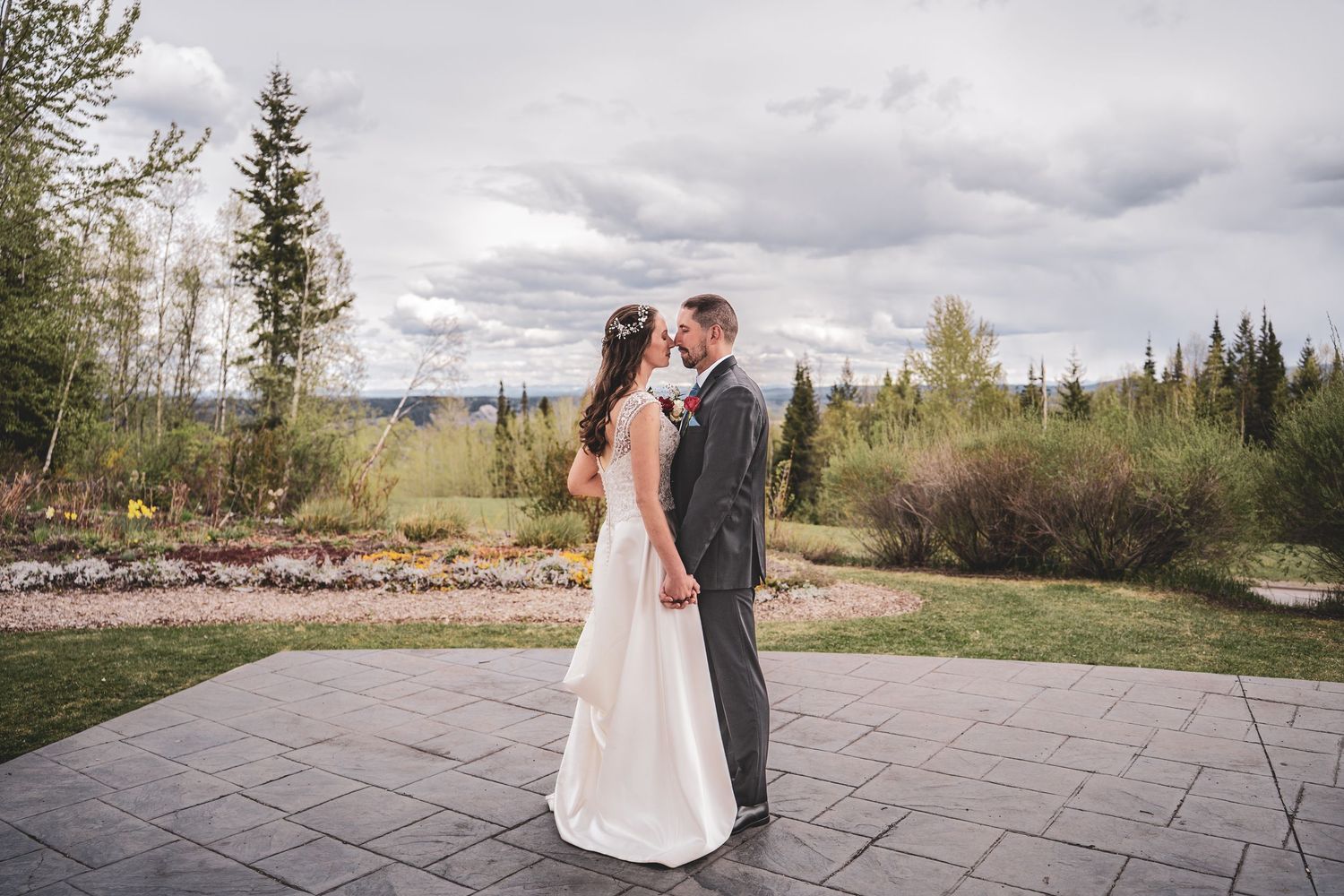 Bride and groom share a tender moment on a stone patio surrounded by trees and mountain views.
