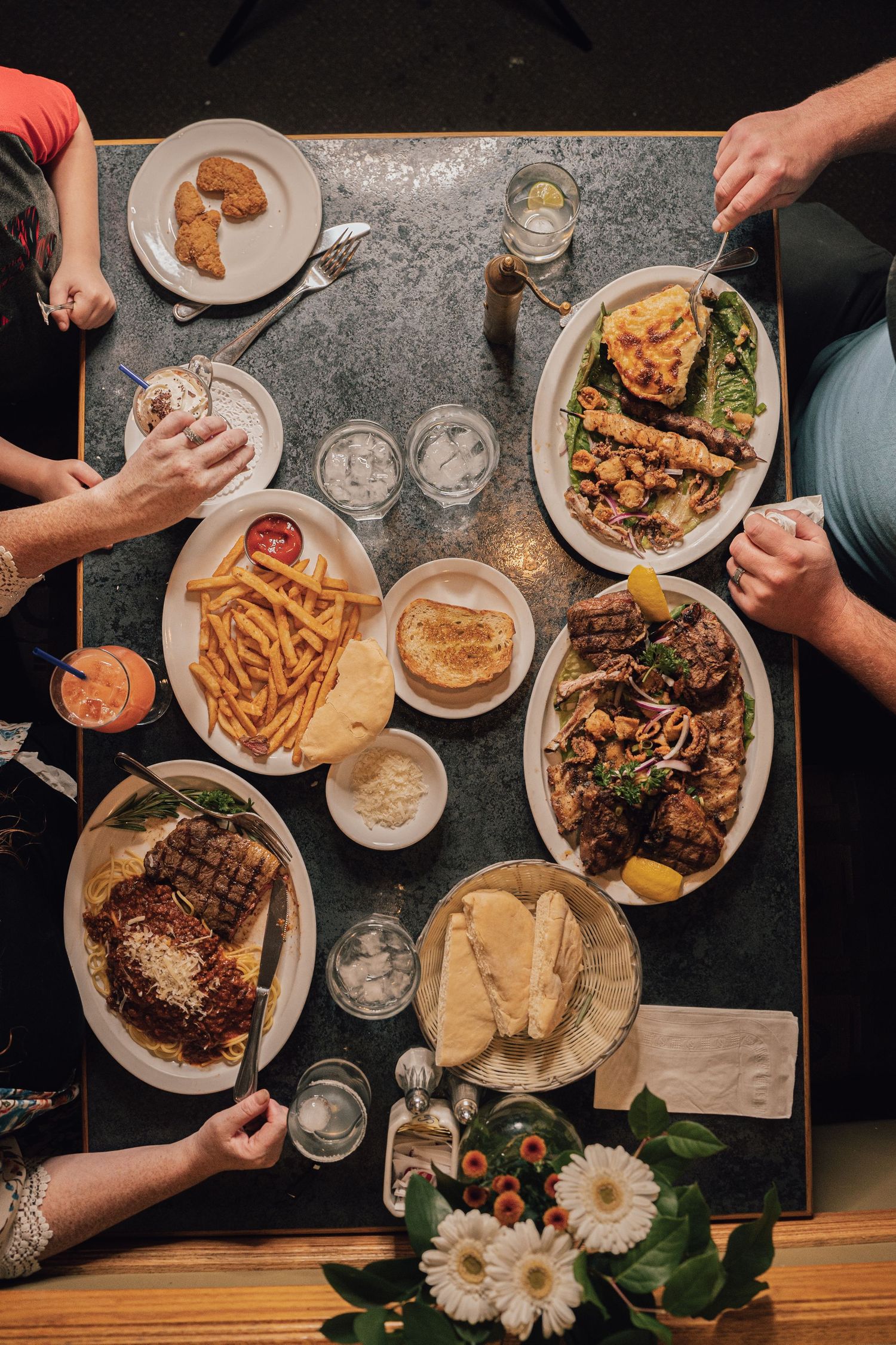 Overhead view of a table spread with fries, steak, grilled meats, and quiche shared by diners.
