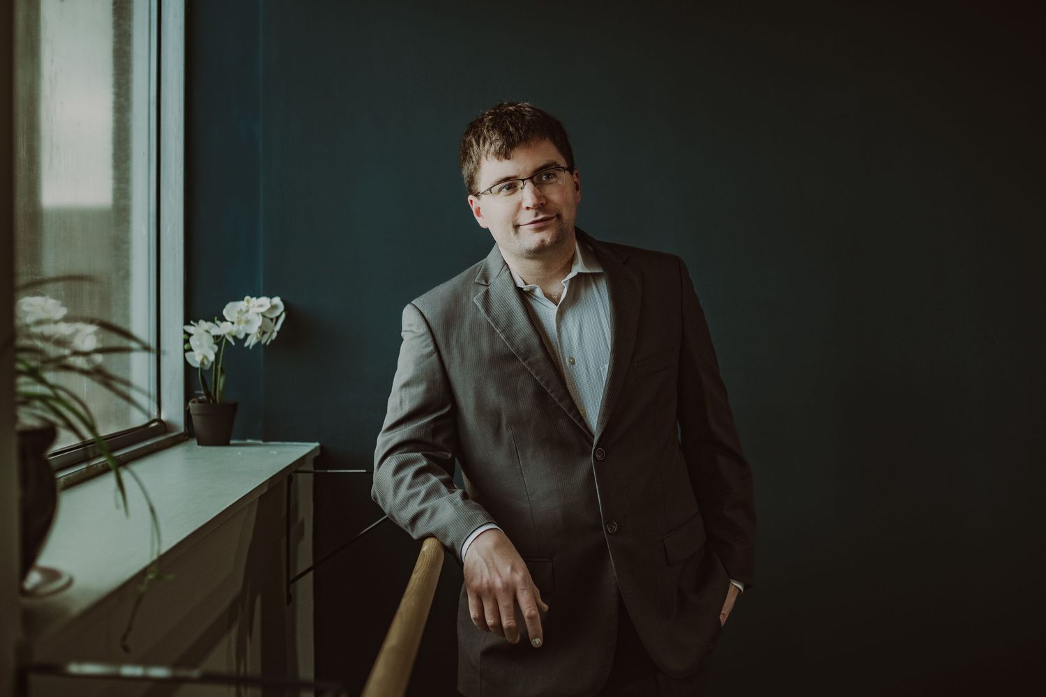 Smiling man in gray suit leaning on chair near window in professional studio portrait during Commercial headshot photoshoot.