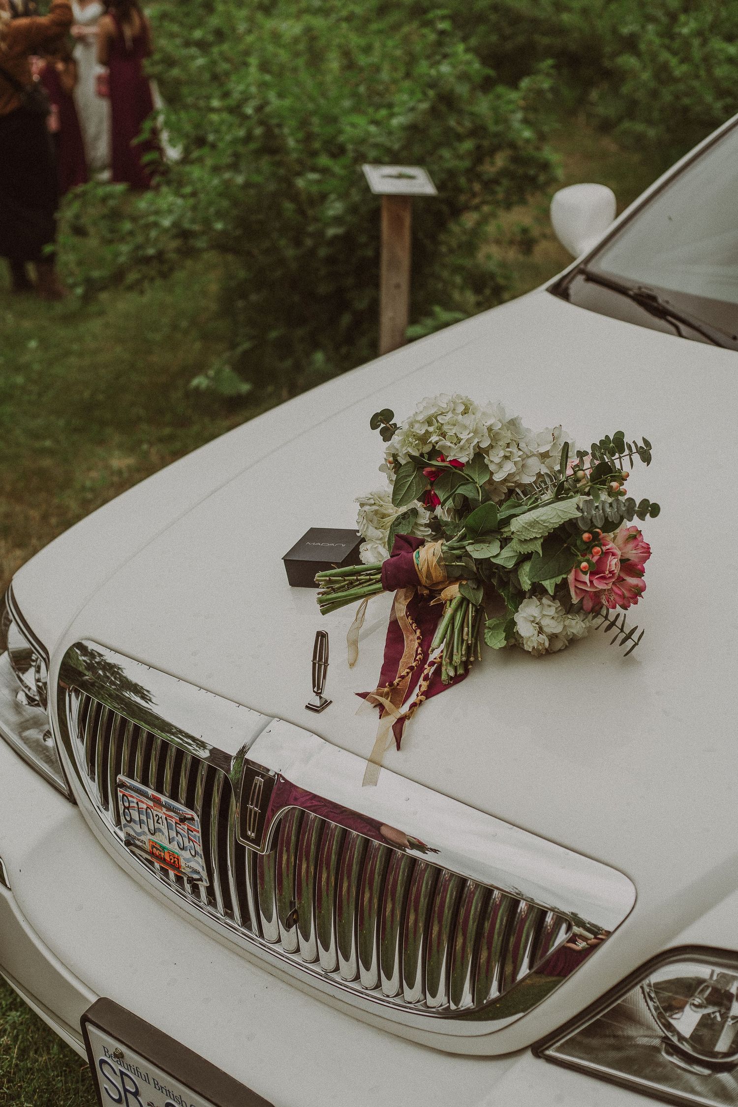 Artistic Wedding Photography of Elegant bridal bouquet of white hydrangeas and pink roses resting on a white luxury limousine hood.